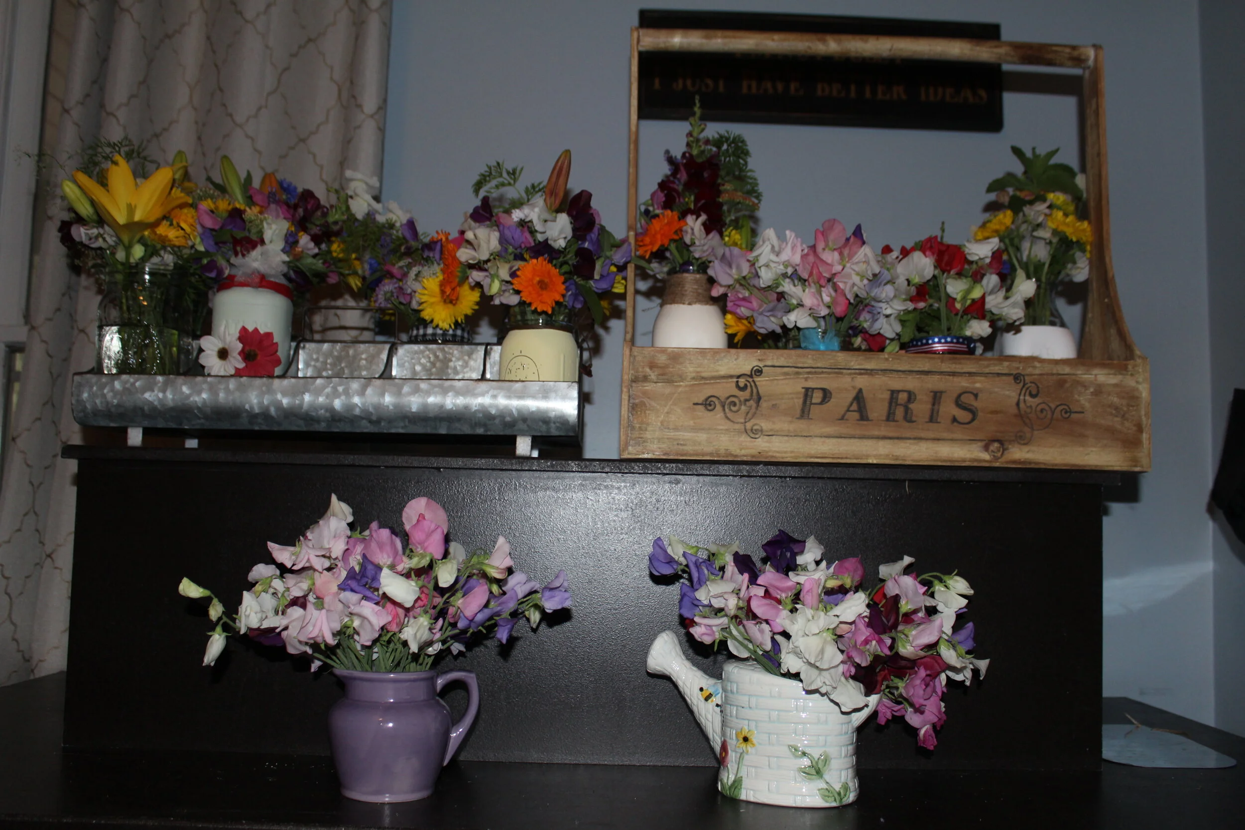 Colorful flower arrangements in vases and containers, including sweet peas, displayed on shelves and a wooden box labeled "Paris."