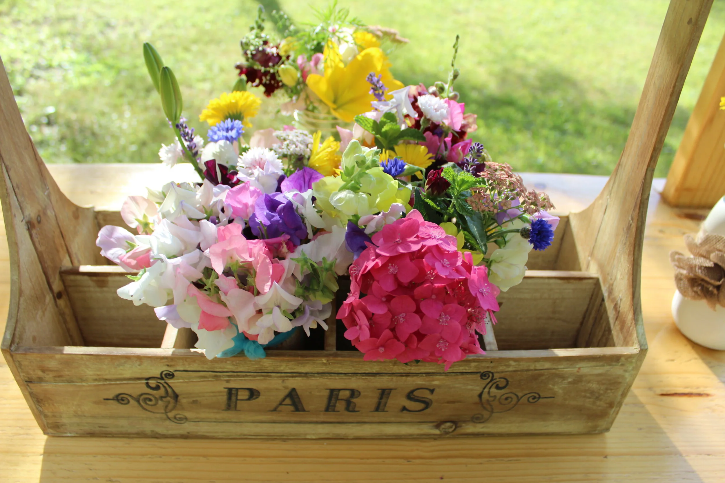 A wooden basket labeled 'Paris' filled with colorful flowers on a wooden surface.