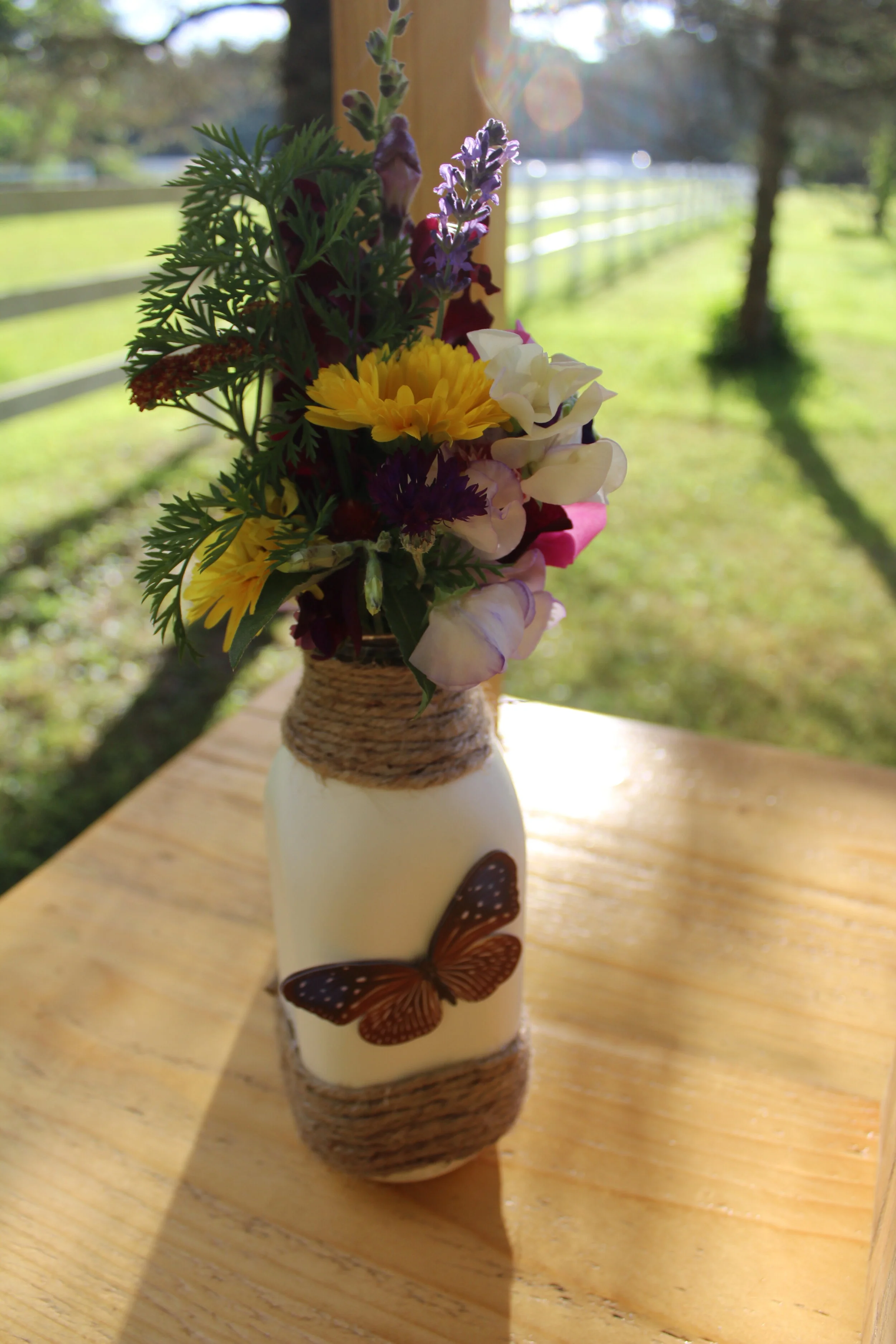 Decorative vase with colorful flowers and butterfly design on wooden table outdoors.