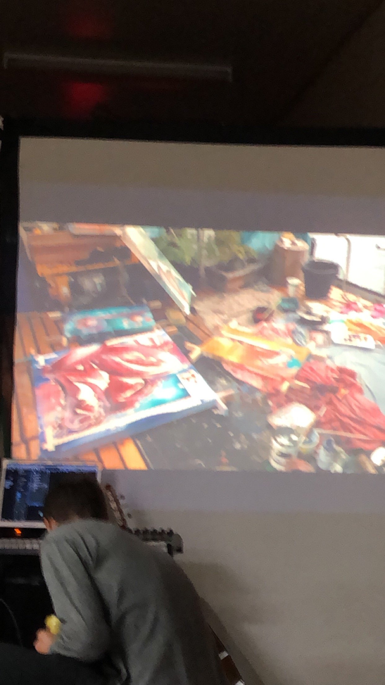 A person working on a computer while a large, projected image of a colorful art display or artwork is visible on the wall or screen in front of them.