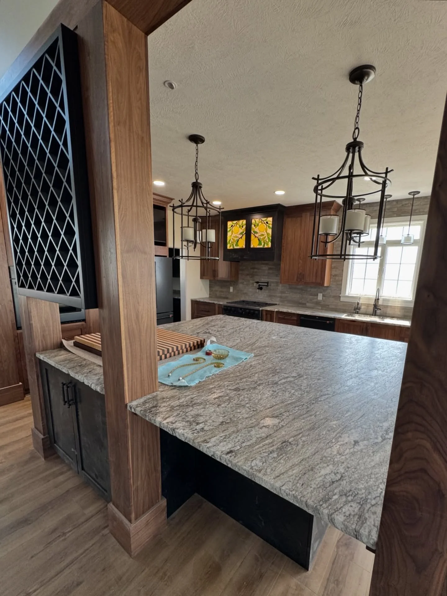 Clear coat walnut kitchen cabinetry to match the wrapped posts and beams (sprayed on site). Installed wine rack and delivered custom cutting boards (on countertop).