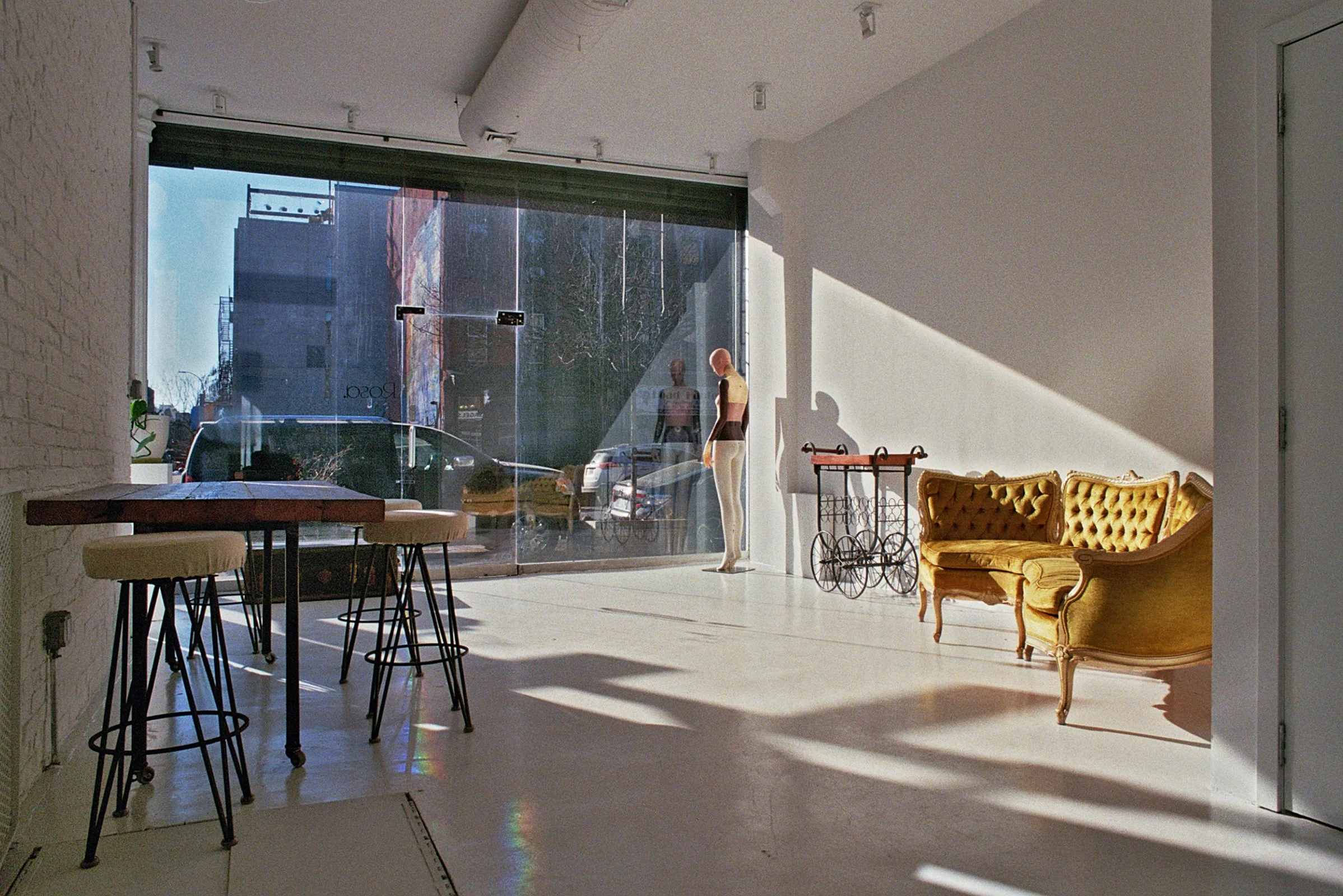 A photography studio with lighting equipment and white umbrellas on tripods on the left, and rolls of purple, green, white, and black paper on rolls on a black holder on the right.