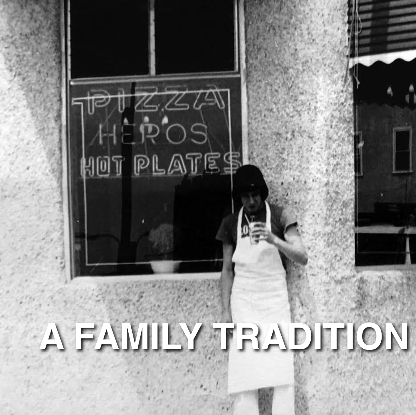 Black and white photo of a woman taking a selfie in front of a restaurant window. The window has a sign reading "Pizza, Hero's, Hot Plates." The woman is wearing a white apron and holding a drink. The image has the caption "A Family Tradition."