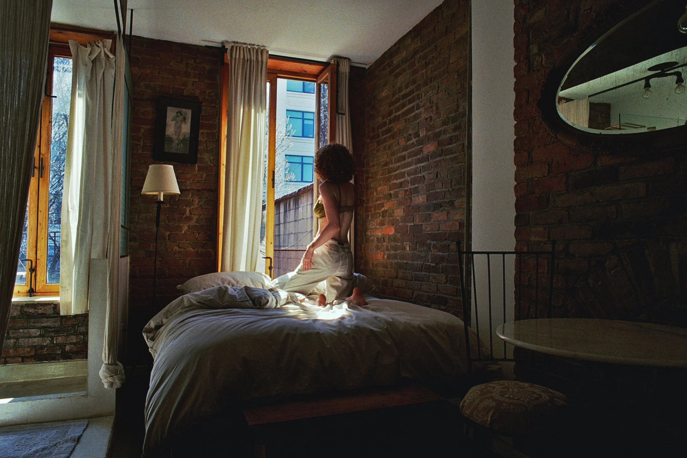 Interior view of a rustic bathroom with exposed brick wall, a vintage mirror, copper pipes, a black sink, and a glass partition.