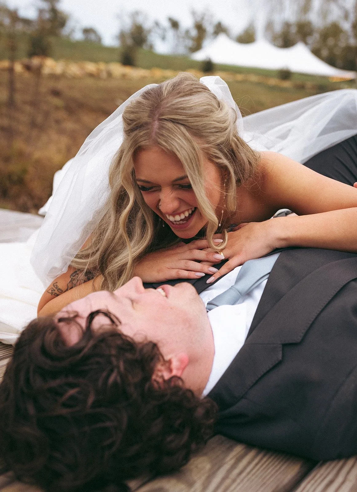 Bride and groom lying on the ground, smiling and gazing at each other, during their wedding photos.