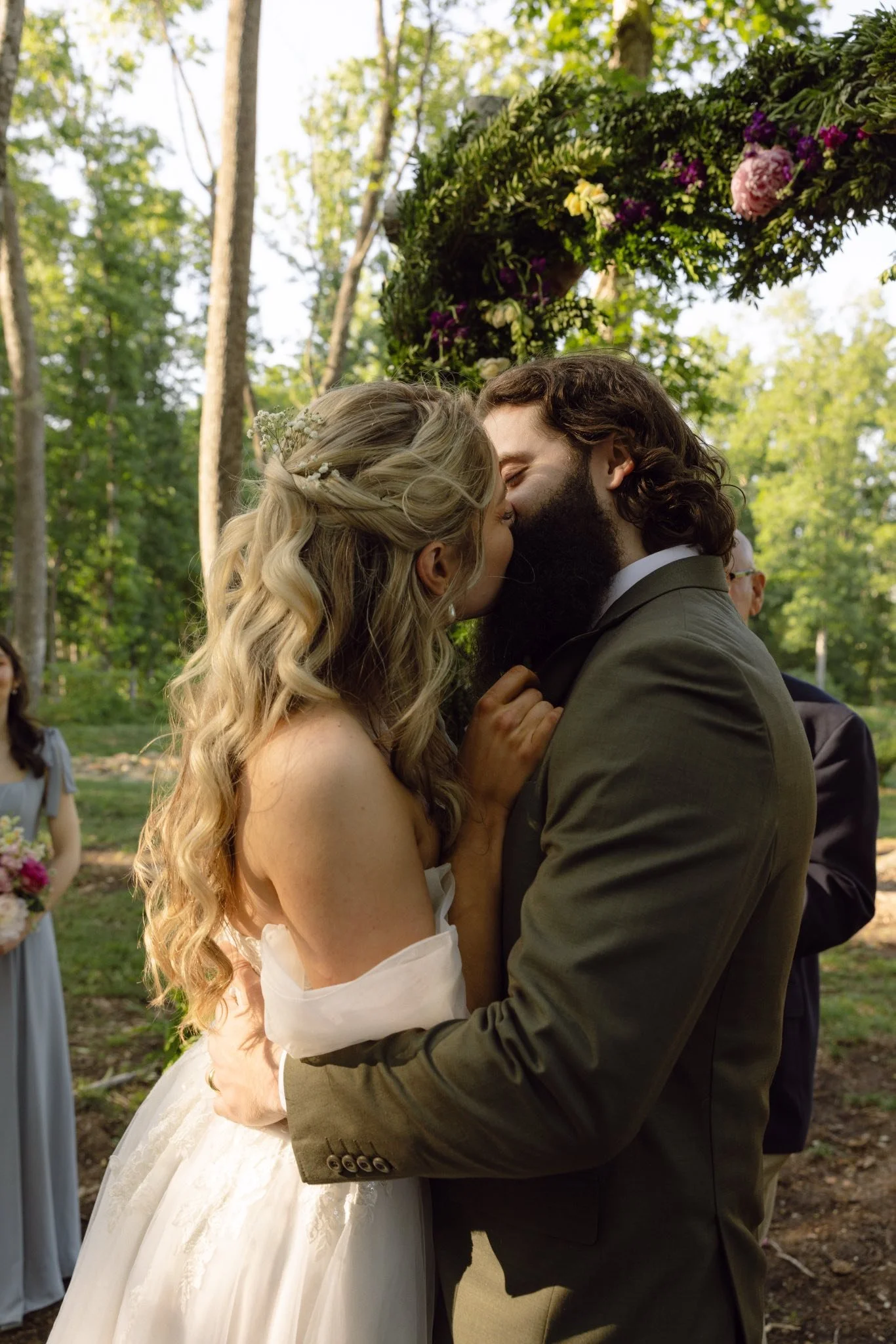 A bride and groom kissing during their outdoor wedding ceremony under a floral arch.