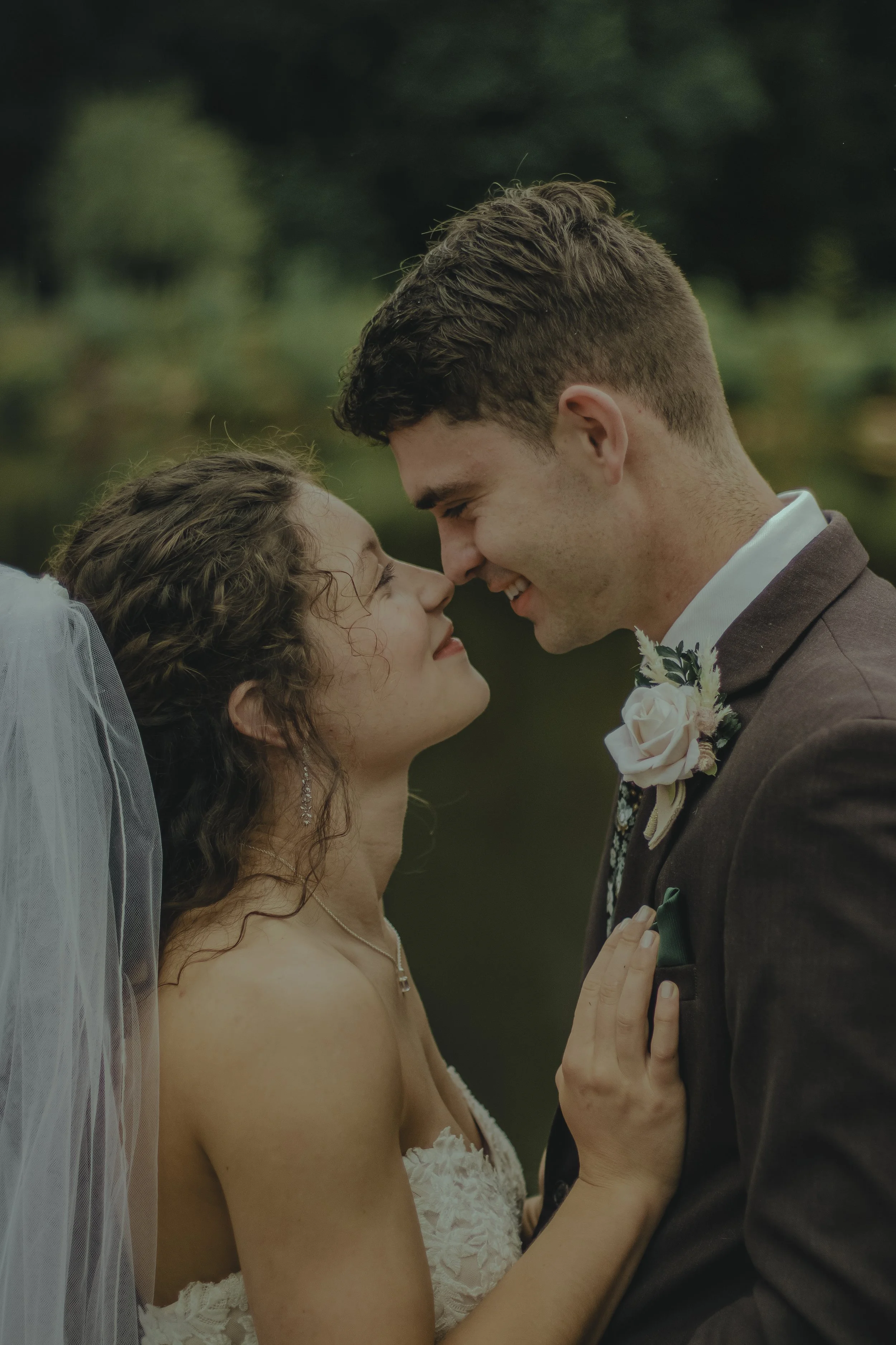 A bride and groom sharing an intimate moment, nose to nose, outdoors during their wedding.