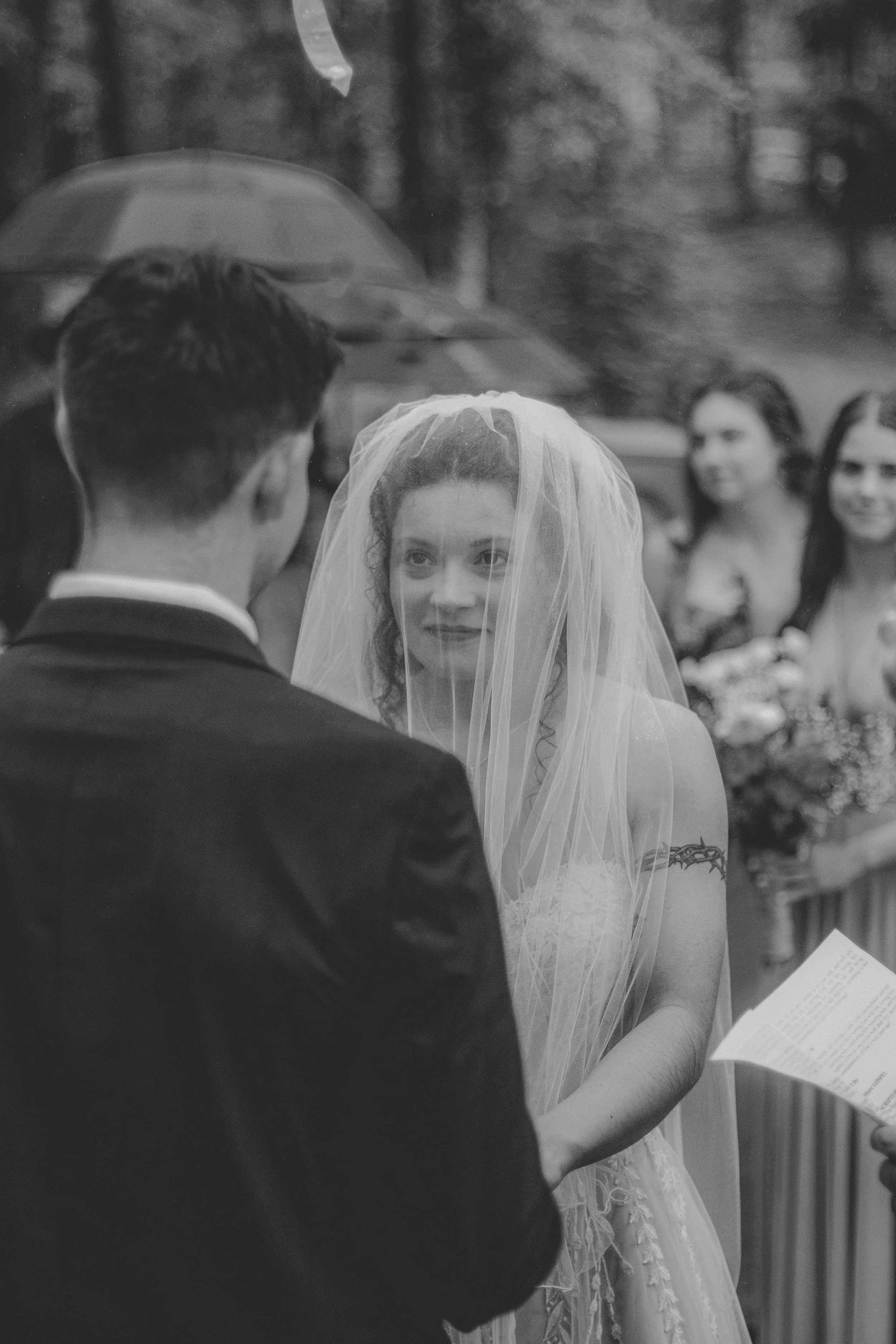 A bride looking at a groom during their wedding ceremony, with bridesmaids in the background.