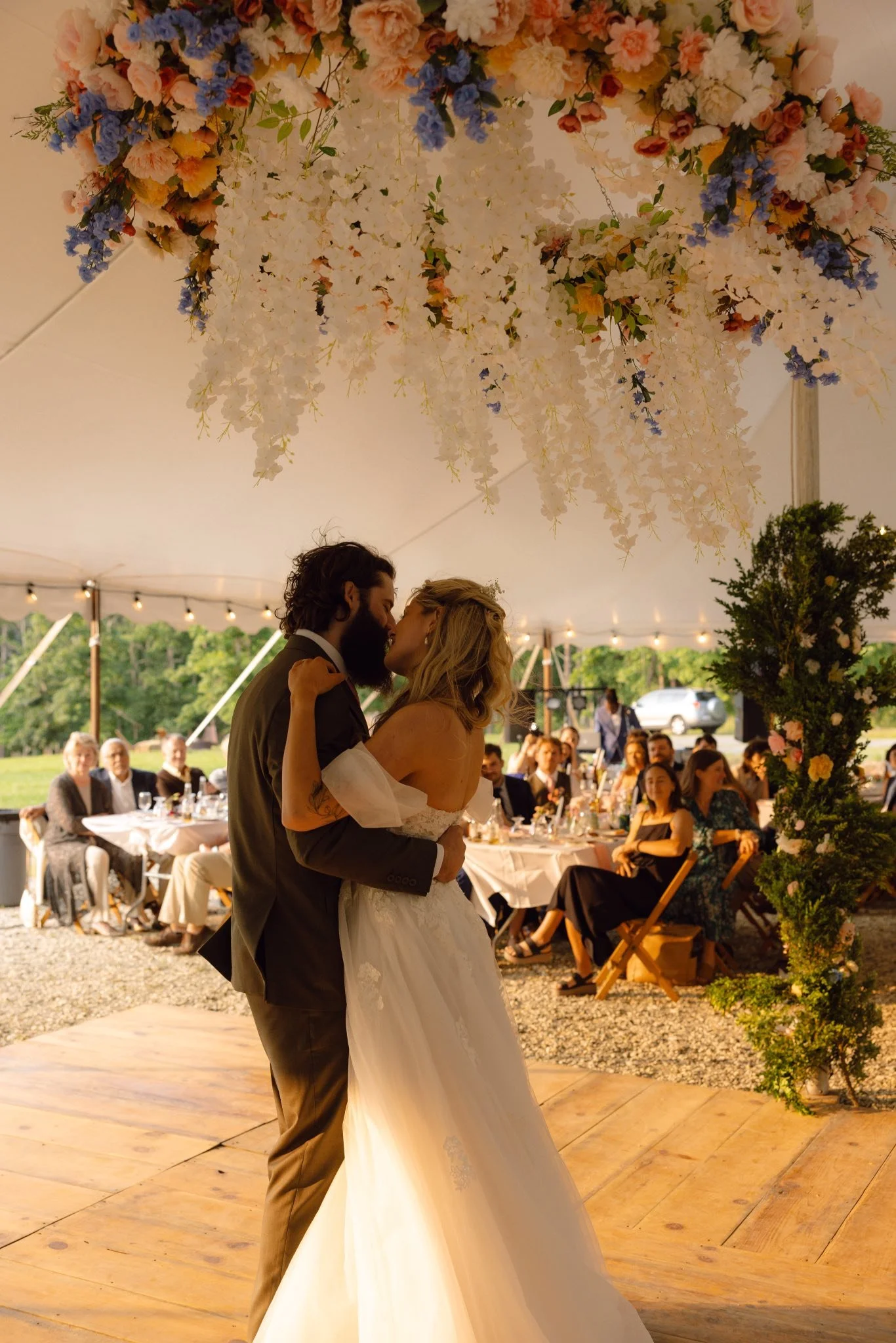 A bride and groom kiss under a decorated floral arch at a wedding reception.