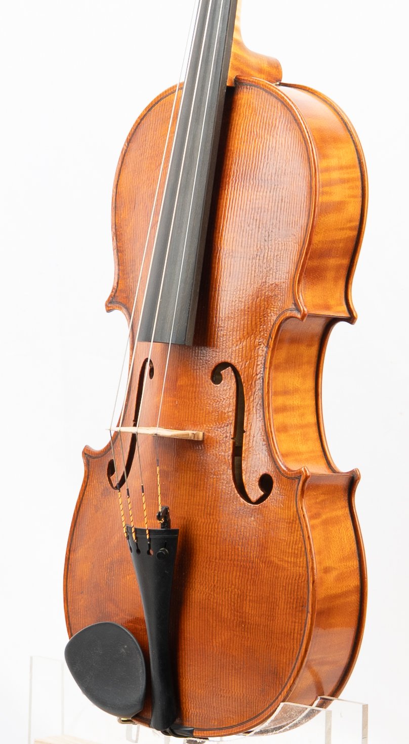 A close-up of a wooden violin with a black chin rest and strings, viewed from a side angle against a white background.