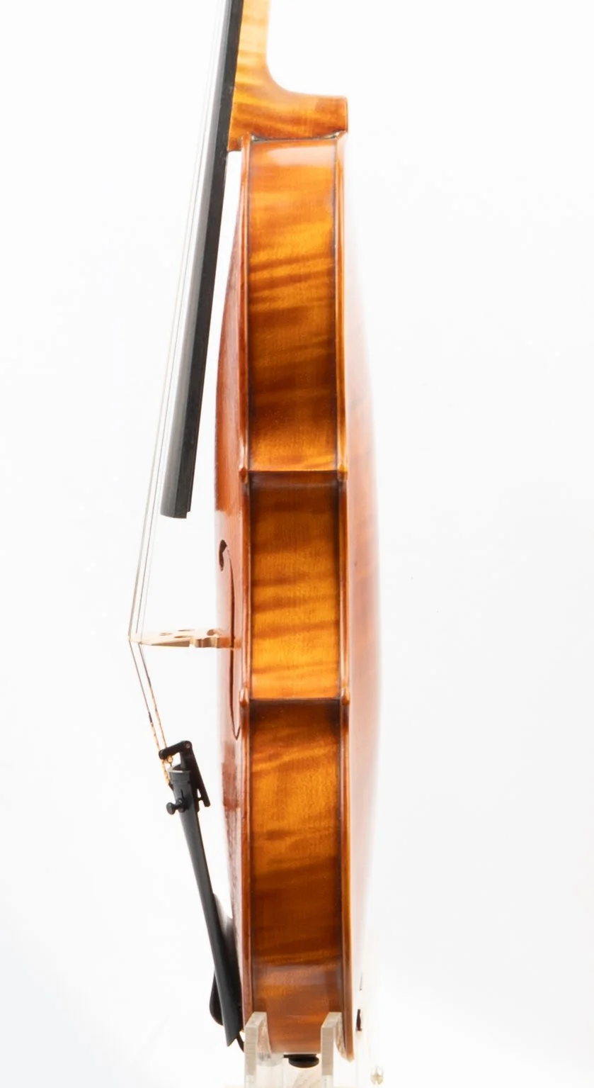 Close-up of an upright wooden grand piano with a black and silver keyboard cover, seen from a side angle against a white background.