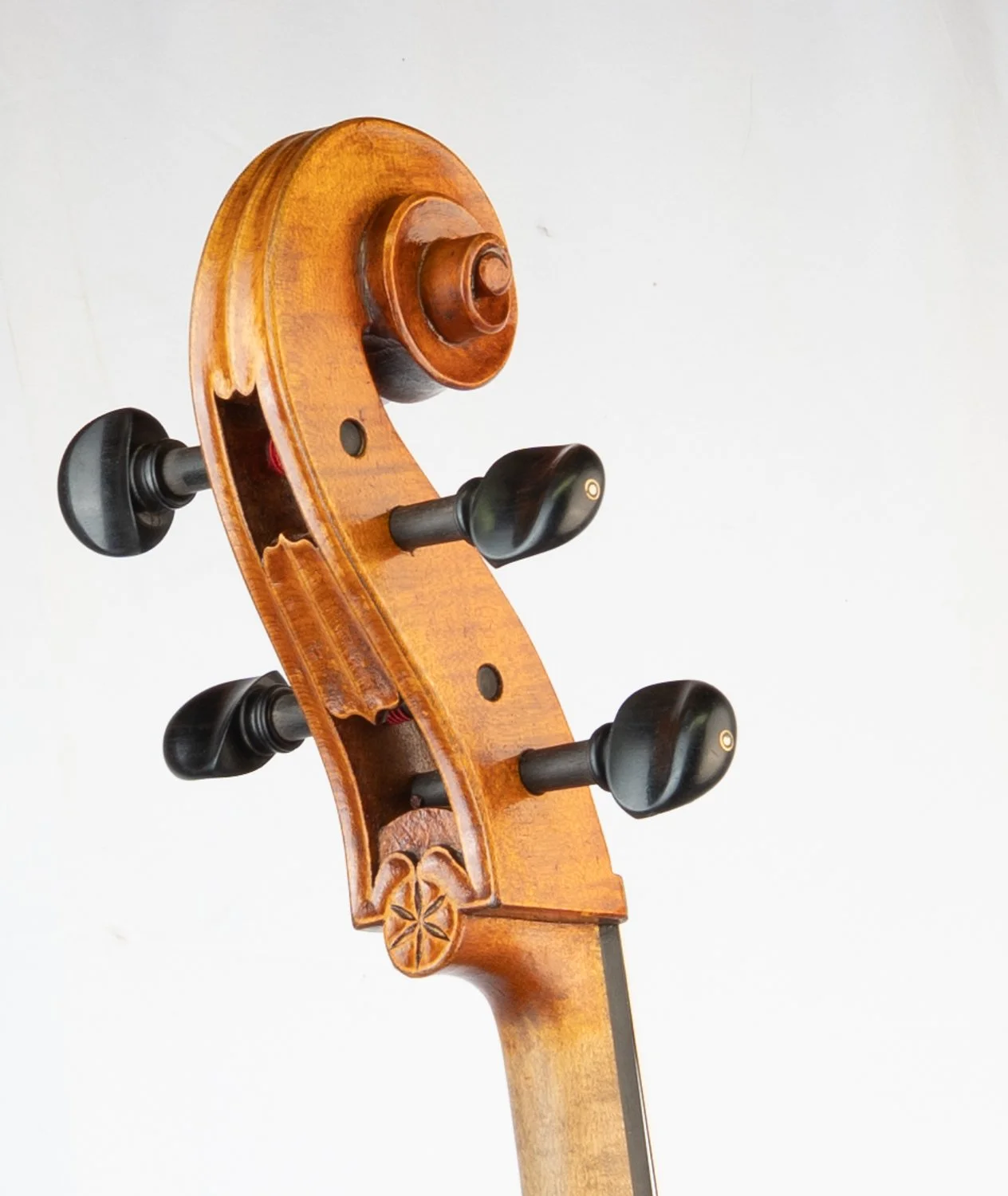 Close-up of the scroll and tuning pegs of a wooden acoustic violin against a plain white background.