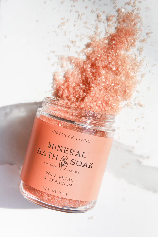 A jar of Circular Living Rose Petal & Geranium Bath Soak ion its side, spilling out the bath soak crystals.
