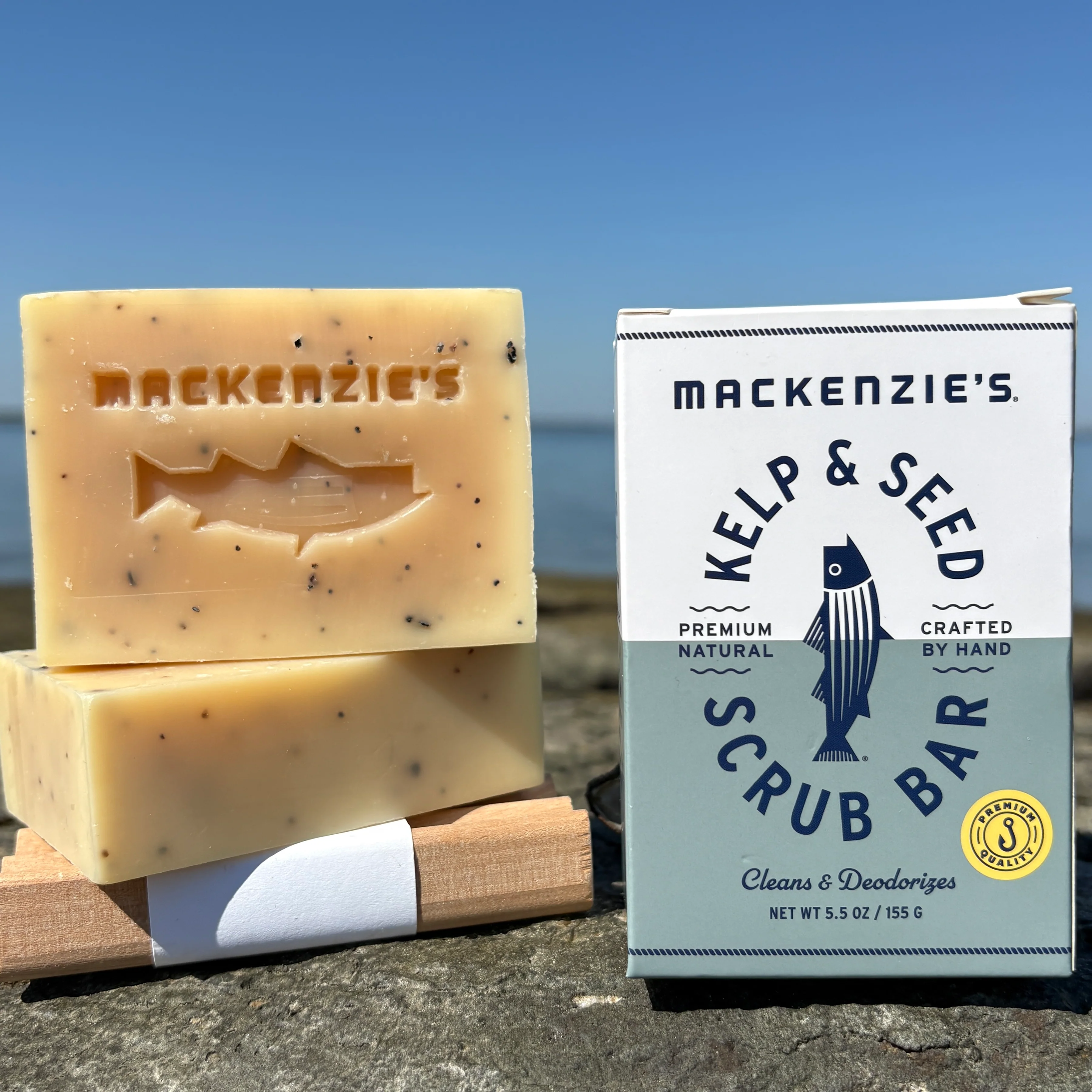 Two unpackaged bar of Mackenzie's Kelp & Seed Scrub Bar next to a packaged bar,.