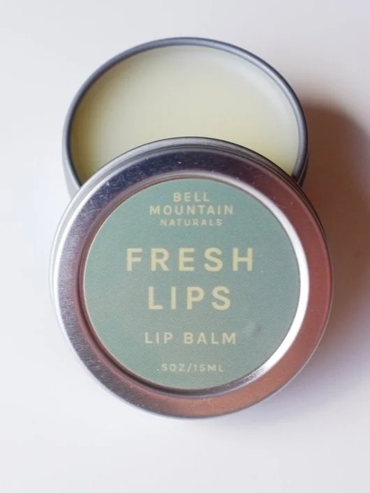 An small silver, open tin containing Fresh Lips Lip balm, with a lid with a green label.