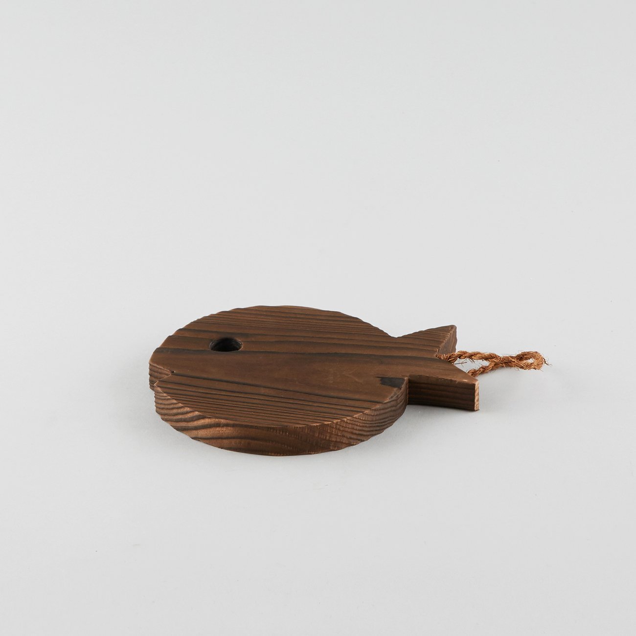 A dark brown stained wooden trivet in the shape of a fish, with a short rope attached at the tail for easy hanging.