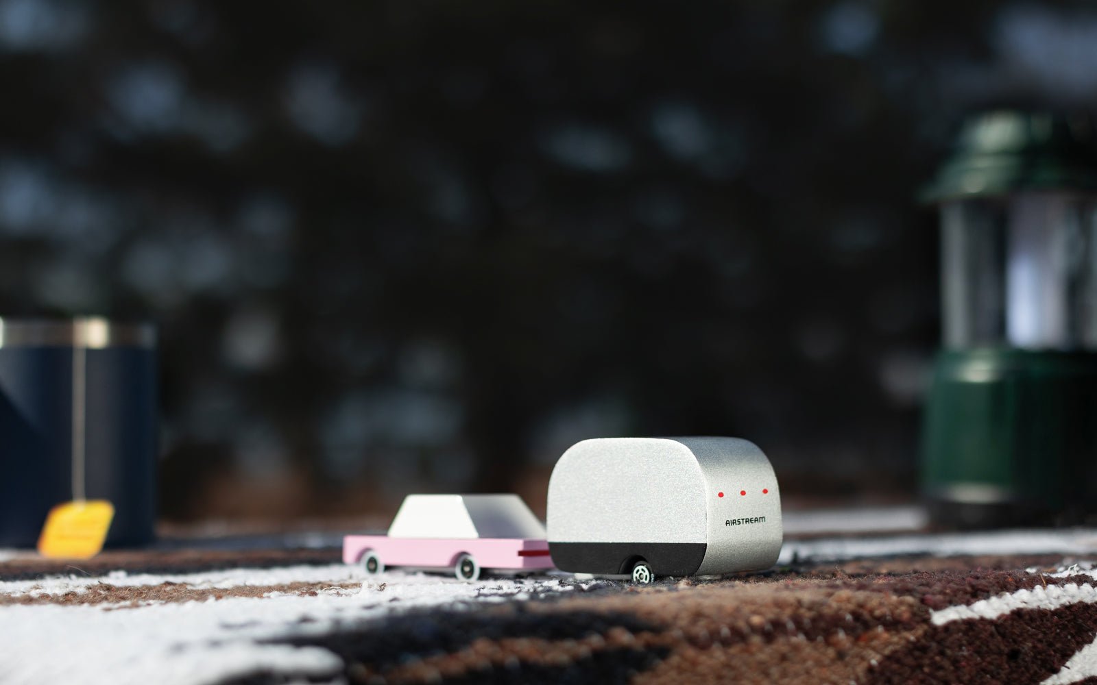A silver and black painted, wooden airstream camper attached to a pink car, on a road way.