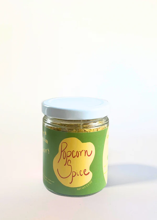 A glass jar with green label with an abstract yellow graphic, the words "Popcorn Spice" in burgundy, and a white lid.