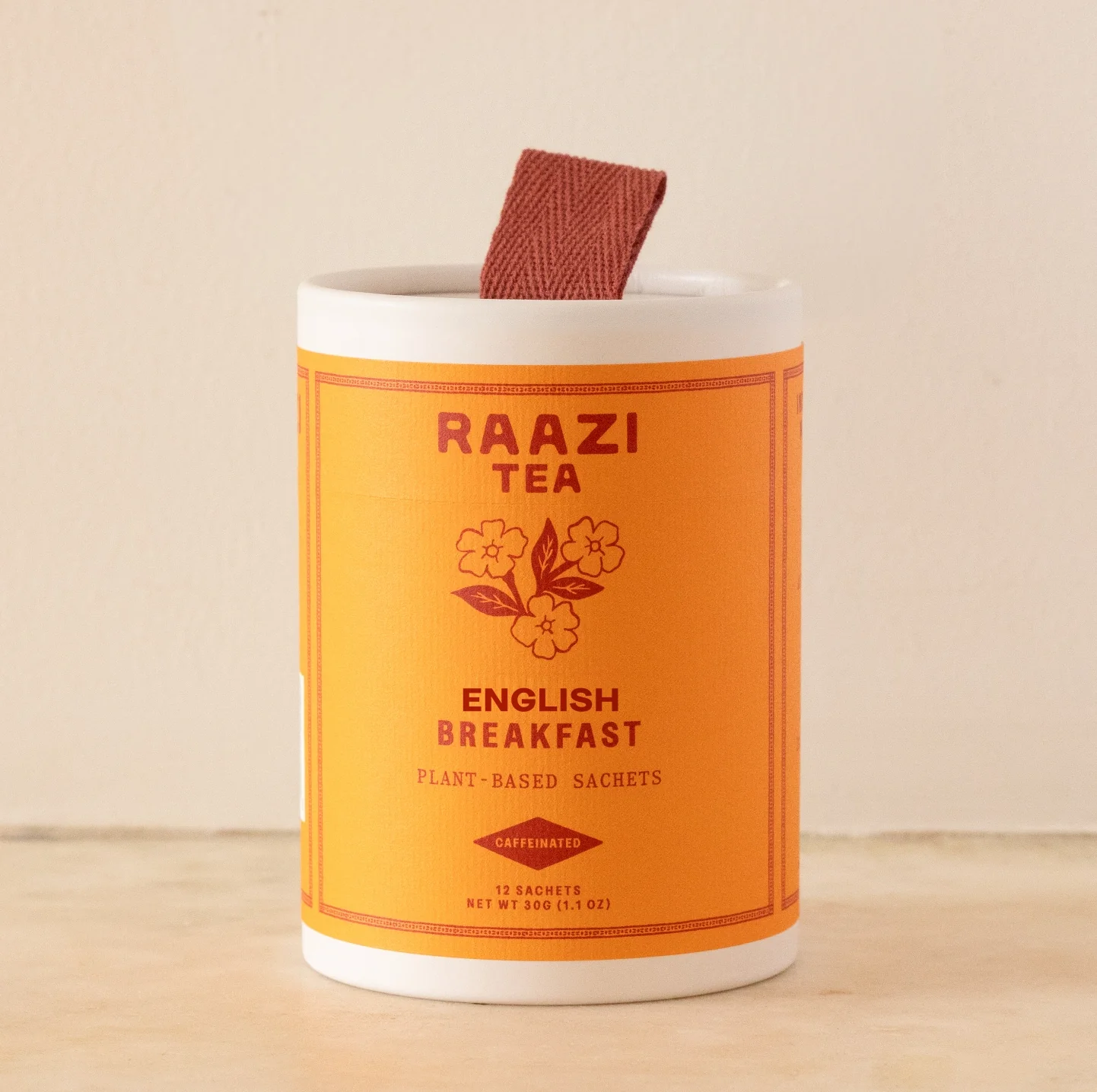 An off white cylinder with a bright orange label and a ribbon loop at the top containing Raazi Tea English Breakfast Tea.