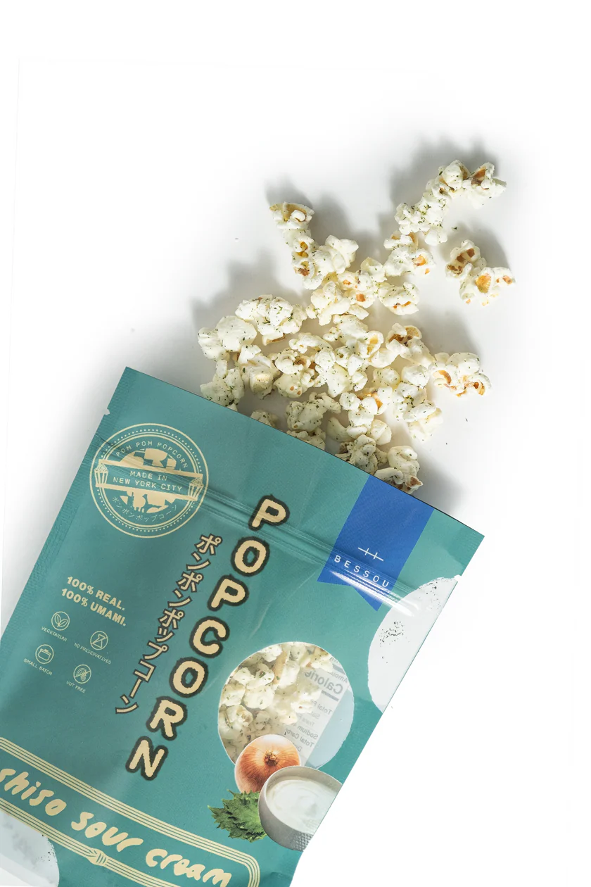 An open, green package of Bessou Shiso Sour Cream Popcorn spilling onto a white surface.