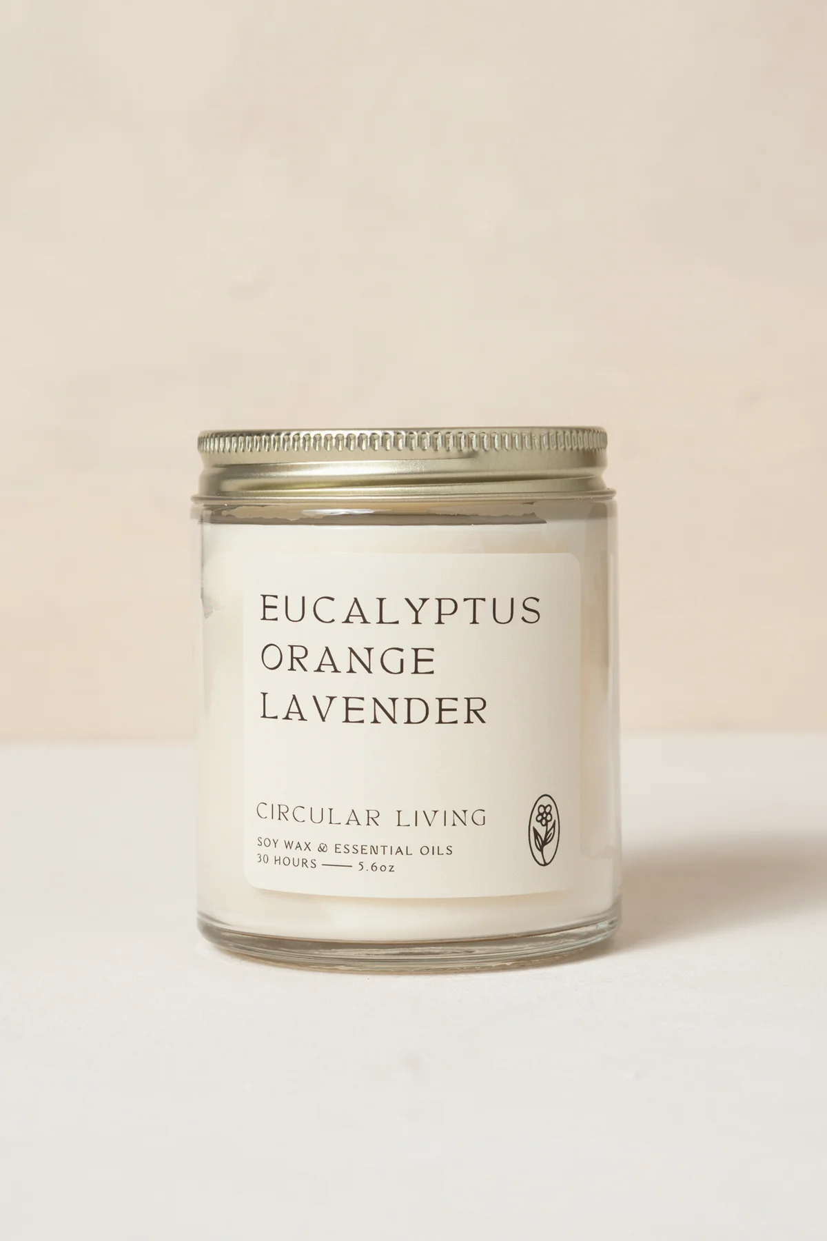 A clear glass jar with white label and gold lid containing Circular Living Eucalyptus Orange Lavender Candle.