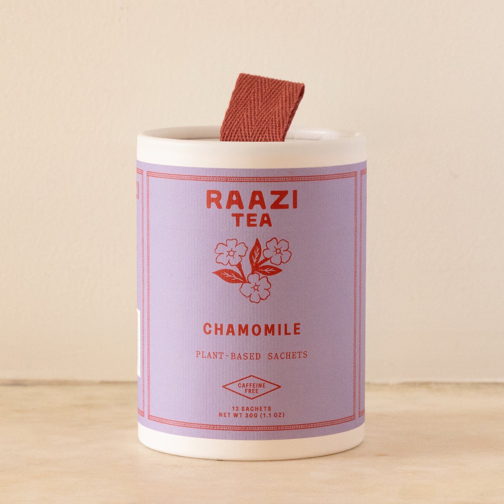 An off white cylinder with a lavender label and a ribbon loop at the top containing Raazi Tea Chamomile Tea.