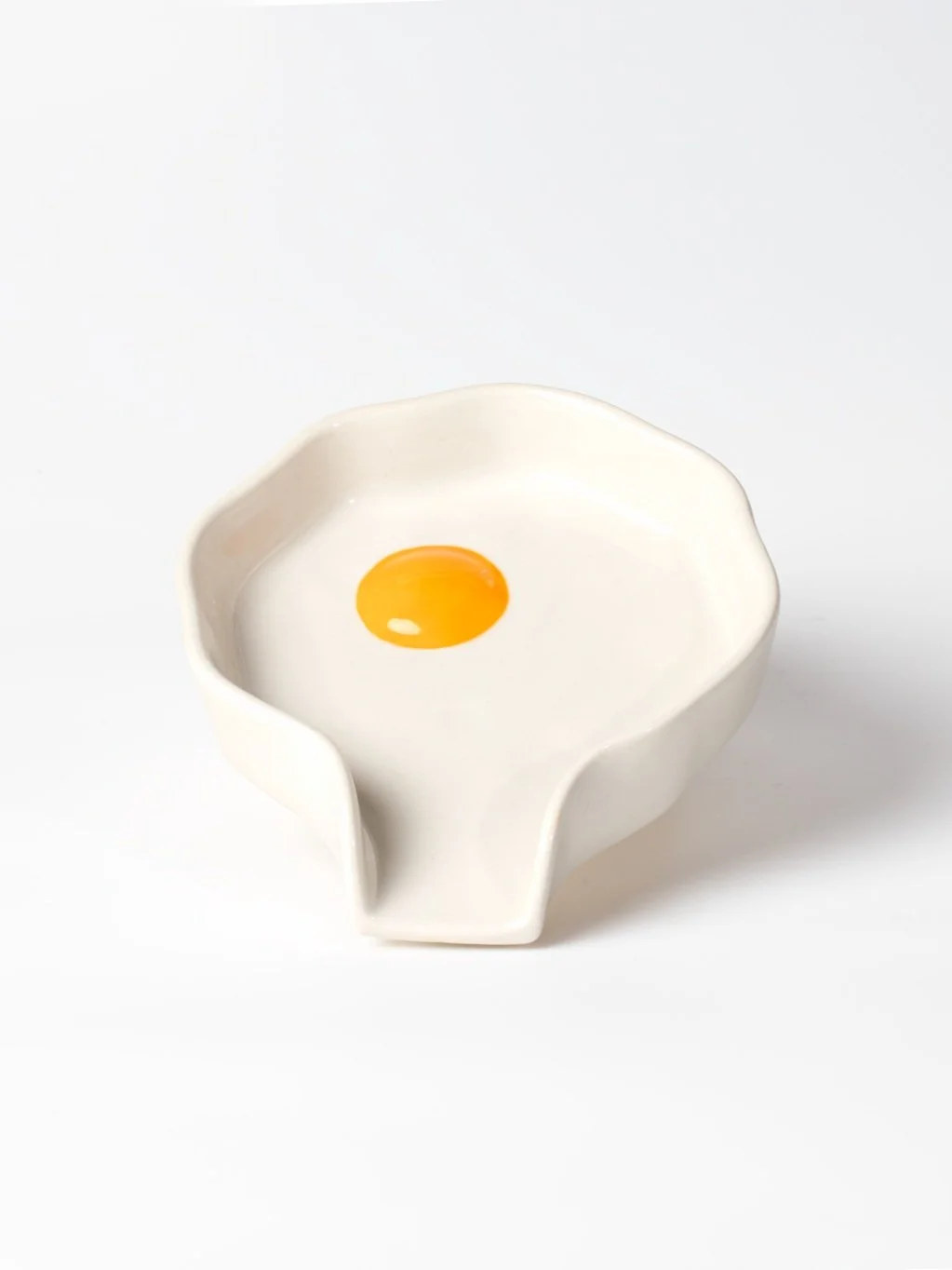 An off white ceramic spoon rest with a yellow yolk near the center.
