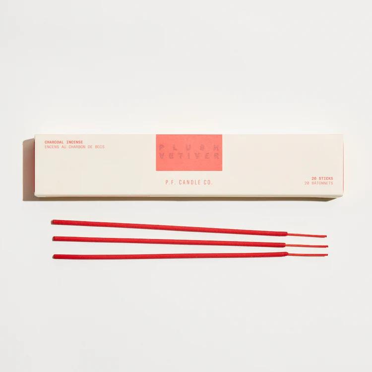 A pale yellow, drawer style box of P.F. Candle Co. Plush Vetiver HI-FI Incense Sticks, above three red incense sticks.