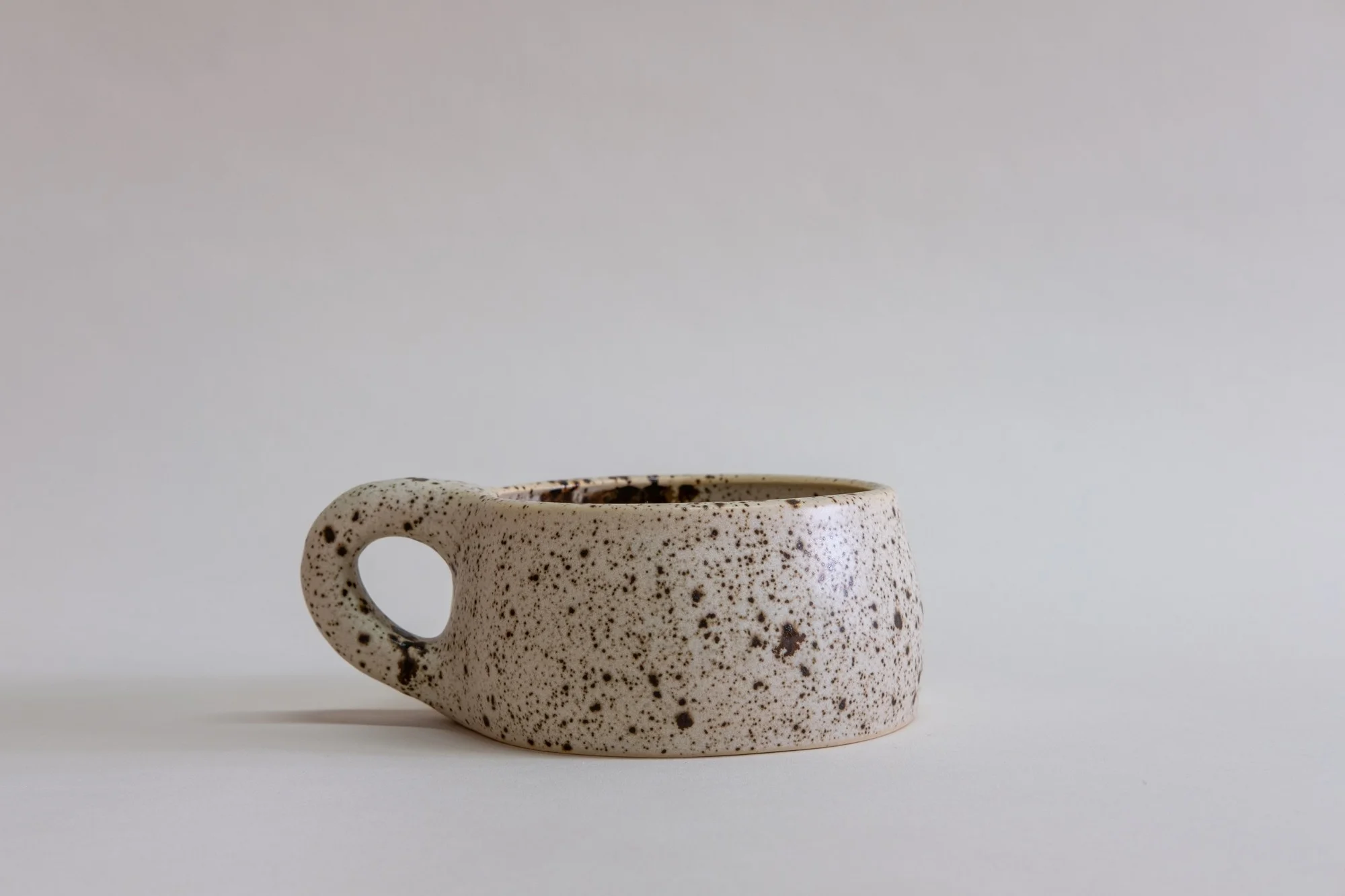 Utility Objects Eggshell Cappuccino Mug, a short, natural colored ceramic mug with brown speckles and a chunky handle.