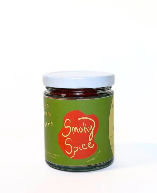 A glass jar with green label with an abstract orange graphic, the words "Smoky Spice" in yellow, and a white lid.