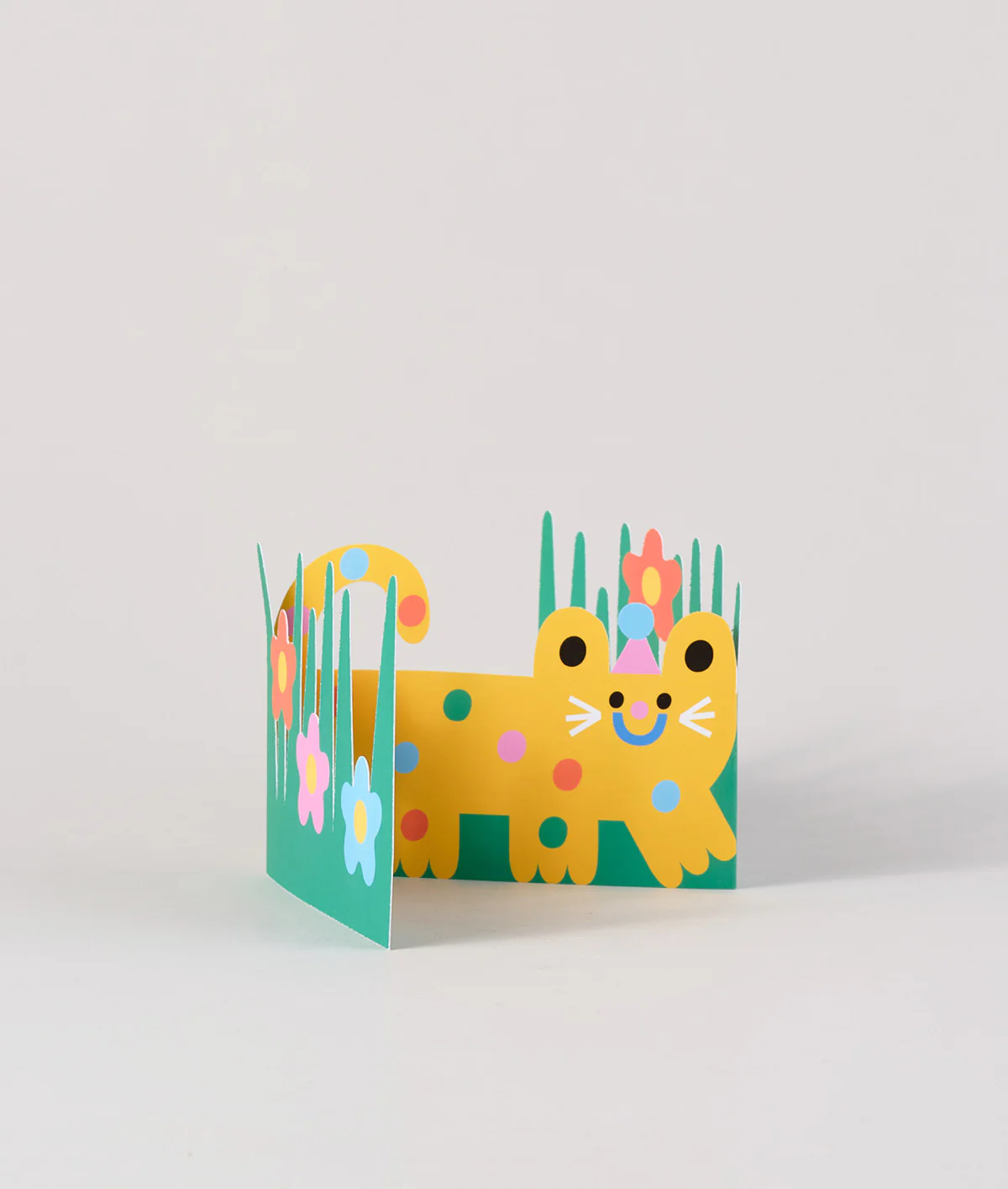 A partially open Cat Fold Out Card, showing a happy yellow cat walking in the green grass and colorful flowers.