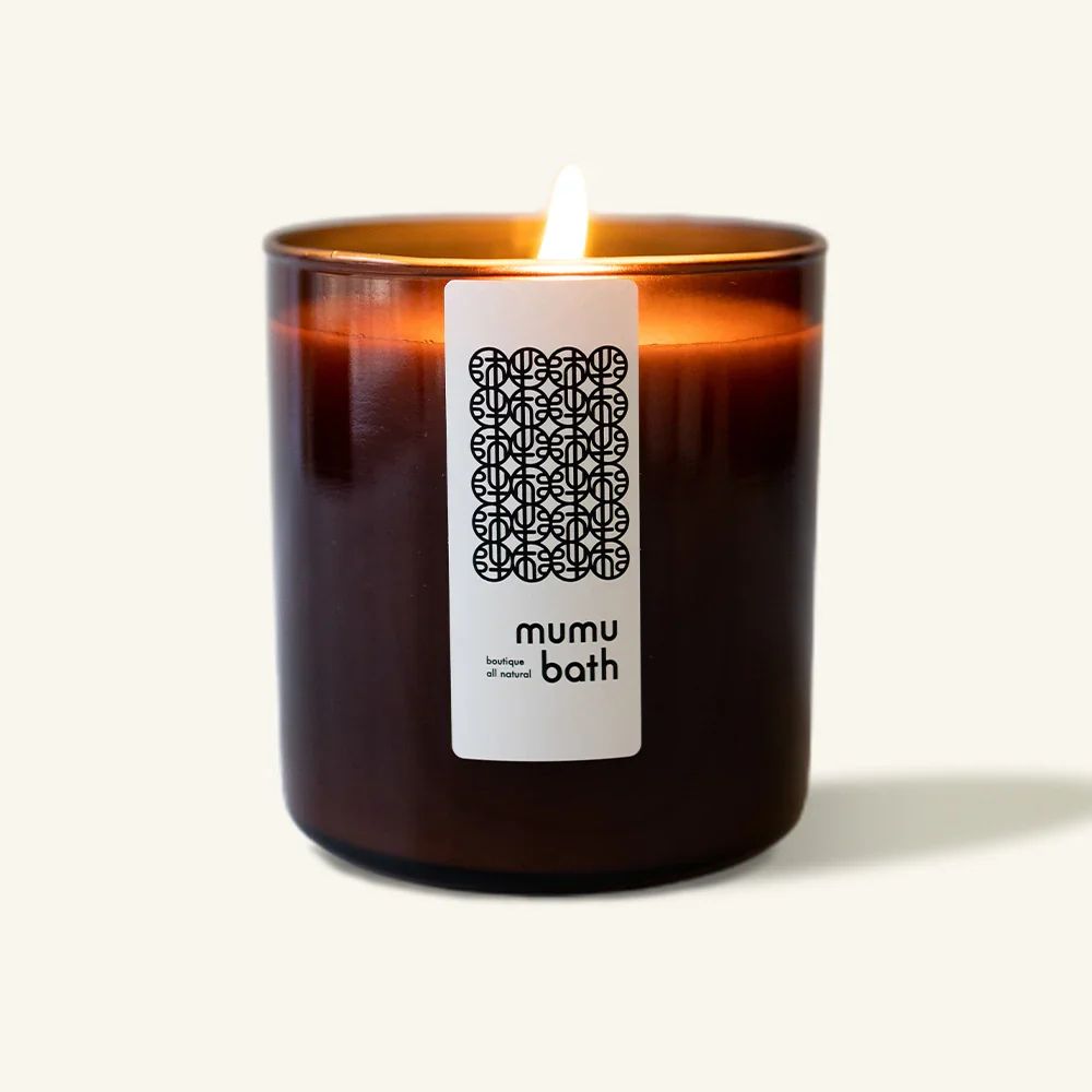 A brown glass jar with a thin white vertical label containing Mumu Bath Earth & Sea Candle.