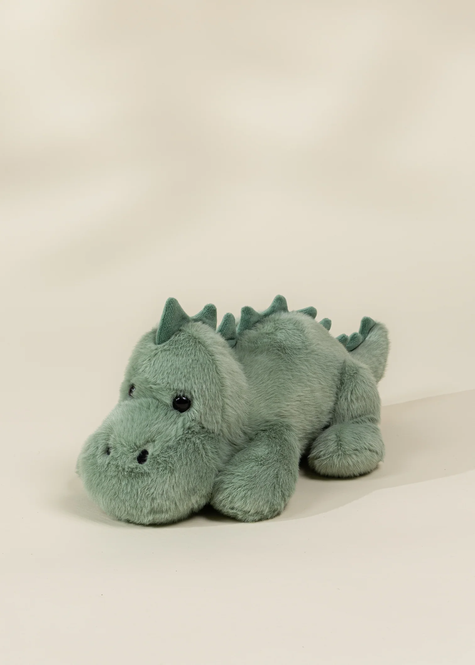 A light green plush Stegosaurus laying on its belly.