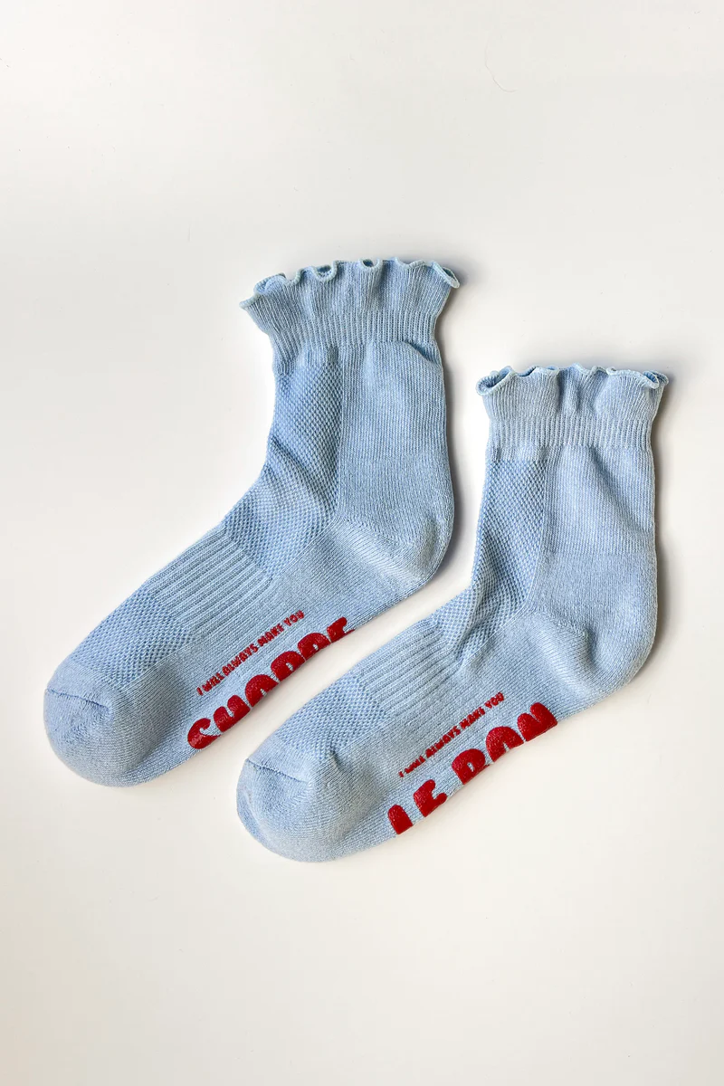 A pair of Le Bon Shoppe Ruffled Hugger Crew Socks in Periwinkle, with red bubbled writing on the soles.