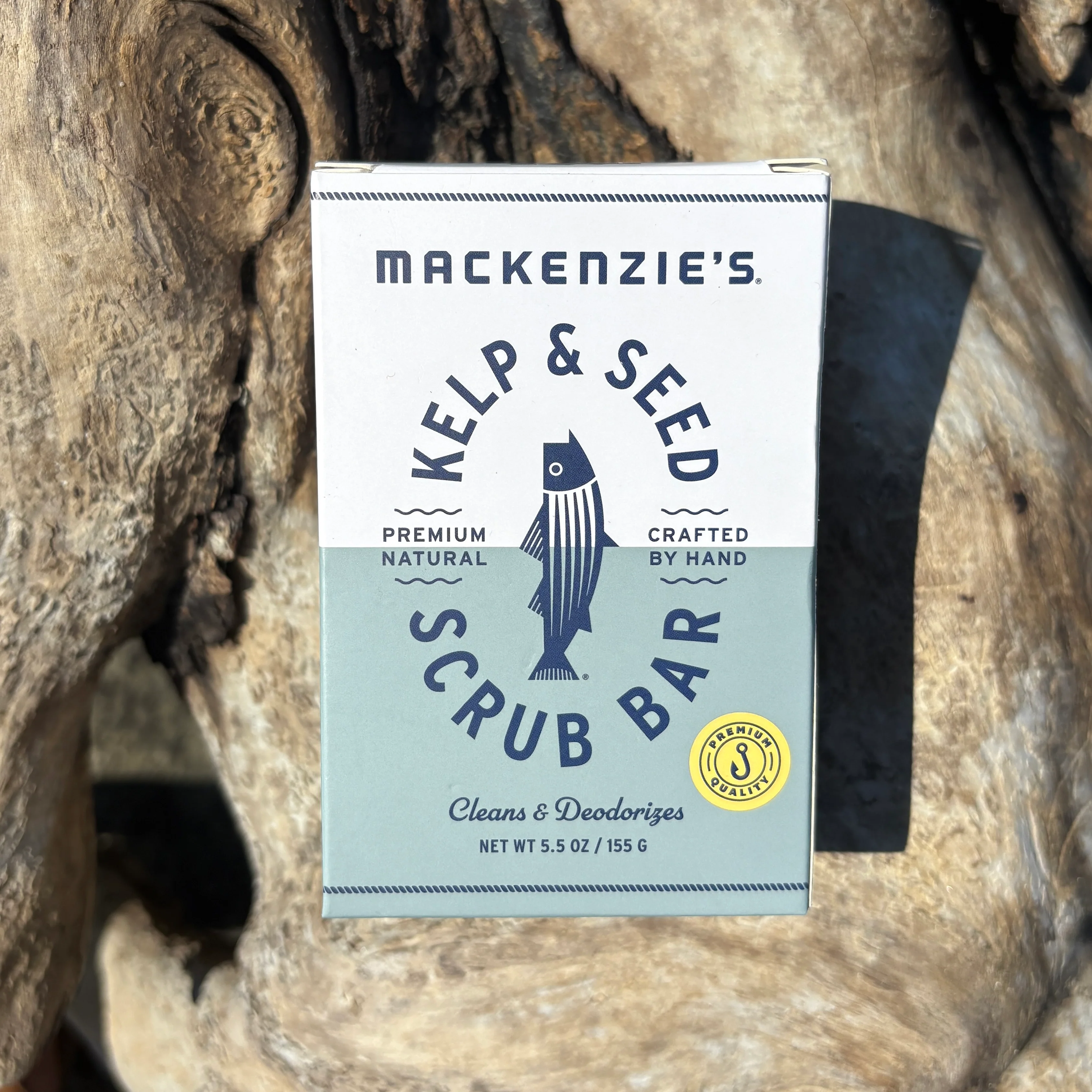 A boxed bar of Mackenzie's Kelp & Seed Scrub Bar resting on large rocks.