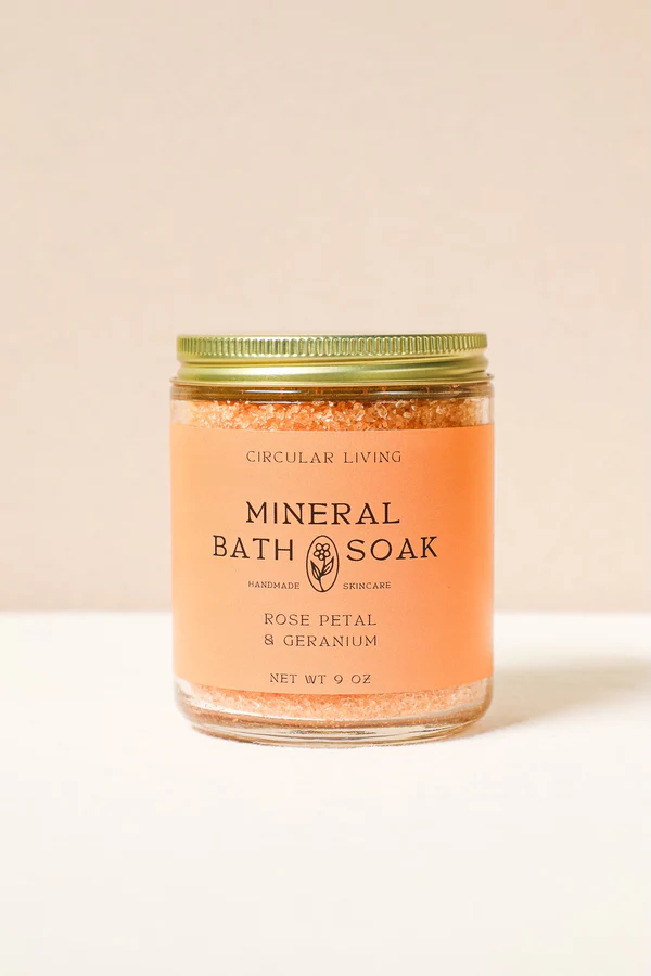 A glass jar with an orange label containing Circular Living Rose Petal & Geranium Bath Soak.
