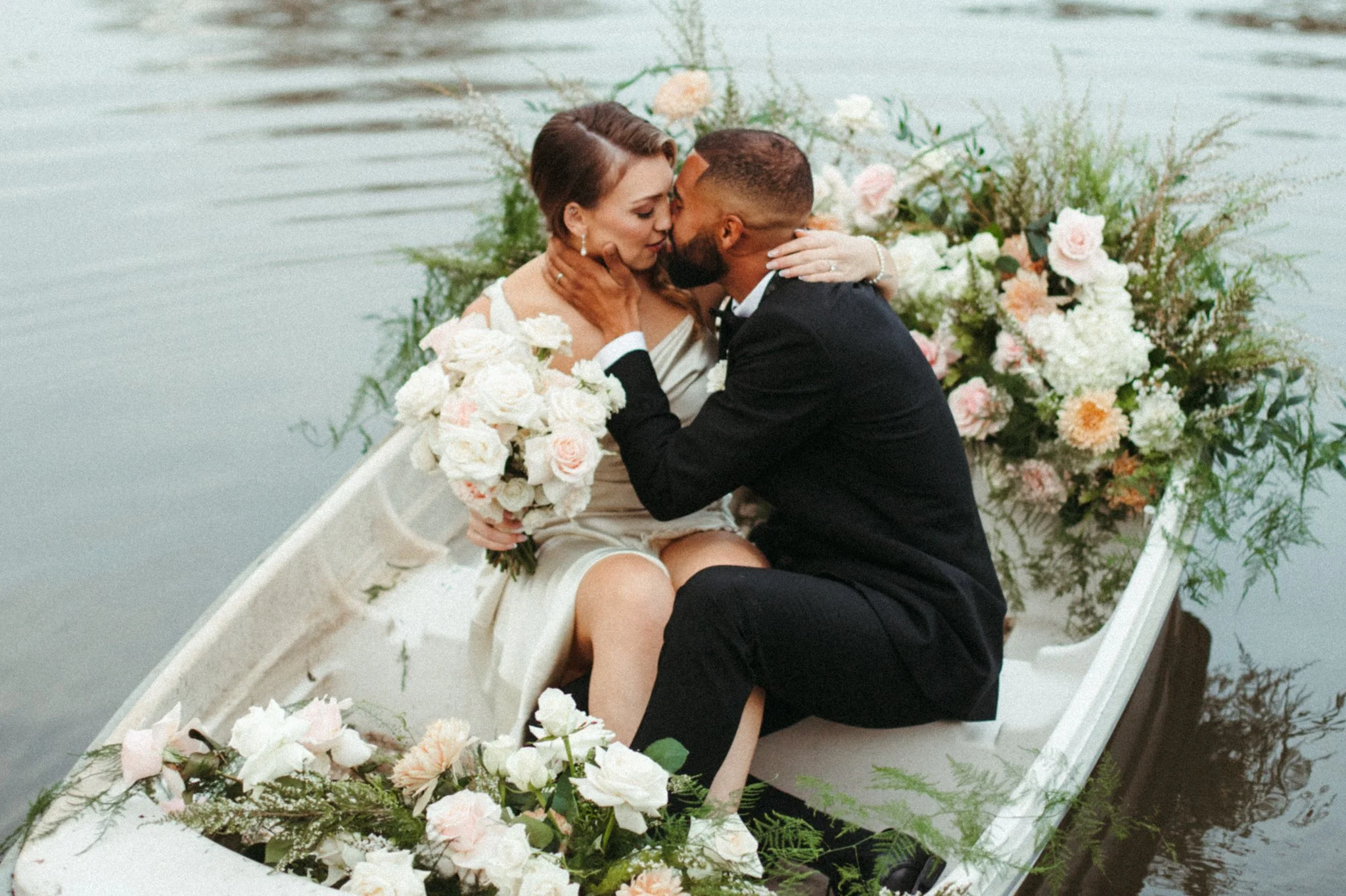 couple kissing on a row boat with flowers on a lake in Sonoma County winery