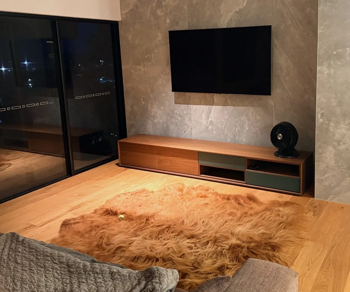 Red Highland cattle hide rug on a timber floor in a modern living room, in front of a wall-mounted TV and sliding glass doors