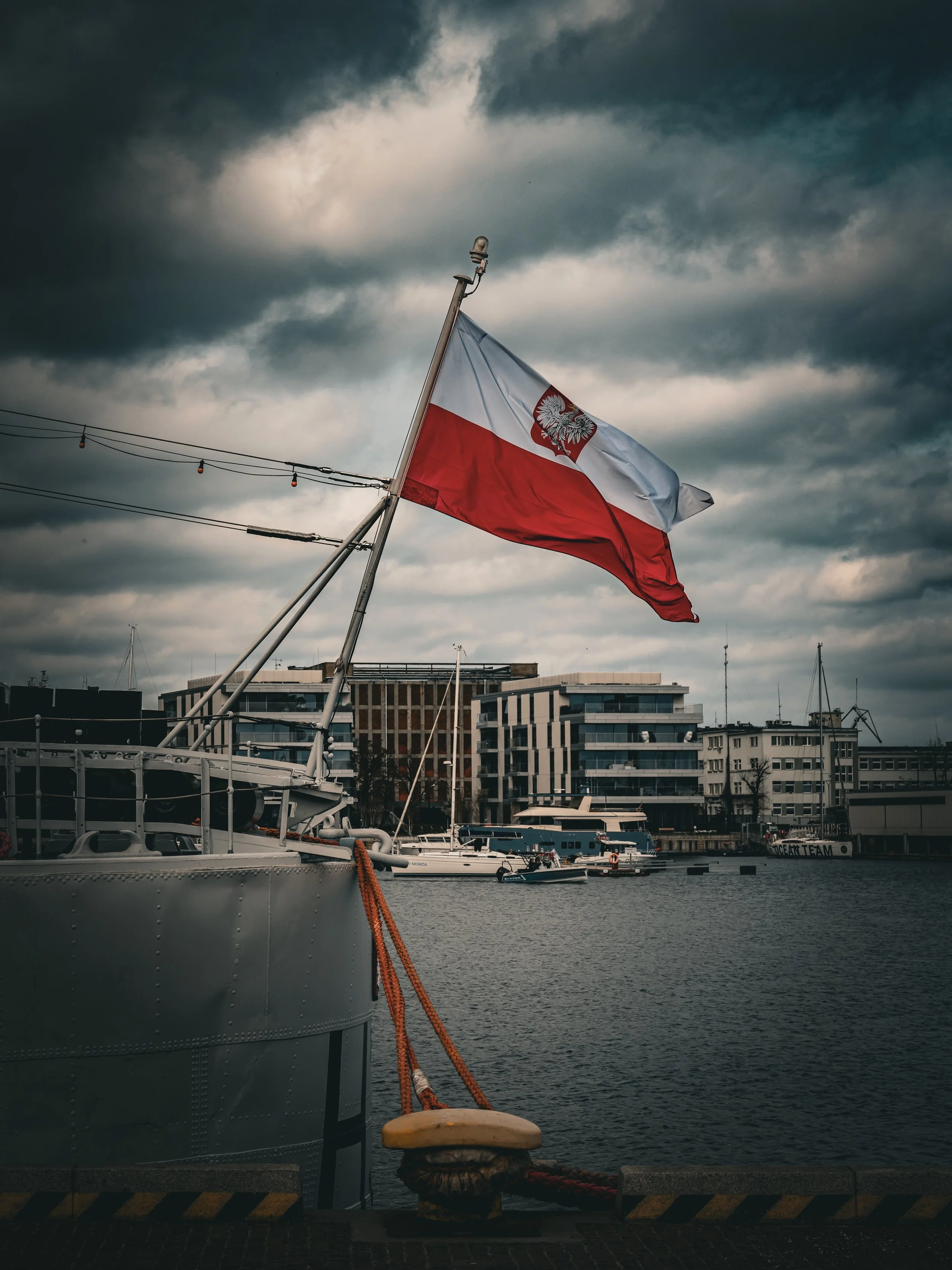 The Polish naval ensign catching the wind against a gathering storm. Gdynia&rsquo;s harbor is deeply rooted in maritime history, and capturing these bold red and white tones against a moody, heavy sky perfectly captures the raw spirit of the Baltic.
