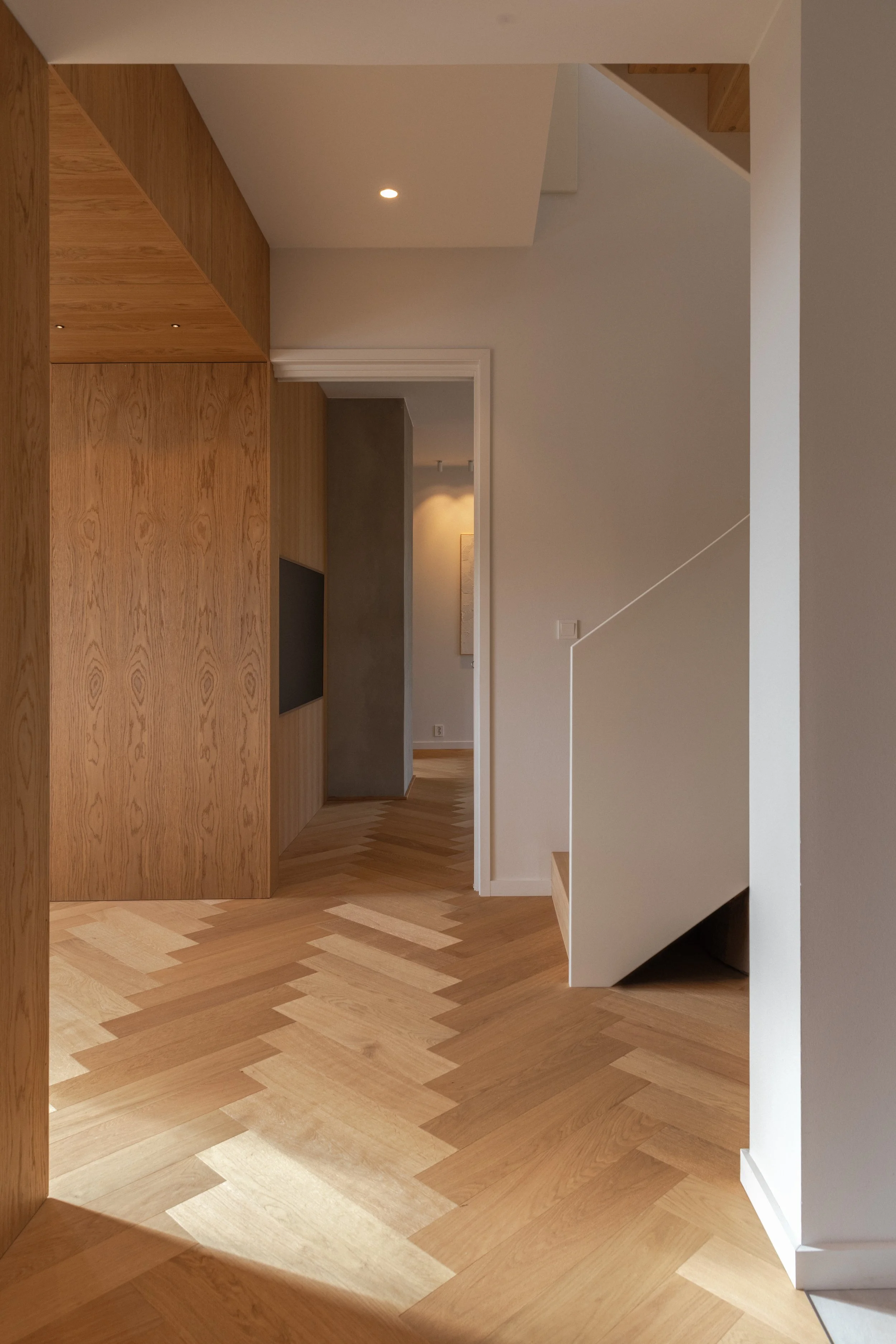 Fiskebensparketten i eik strekker seg sømløst gjennom hele etasjen. I tv-stuen er tv-en integrert i funksjonsveggen.