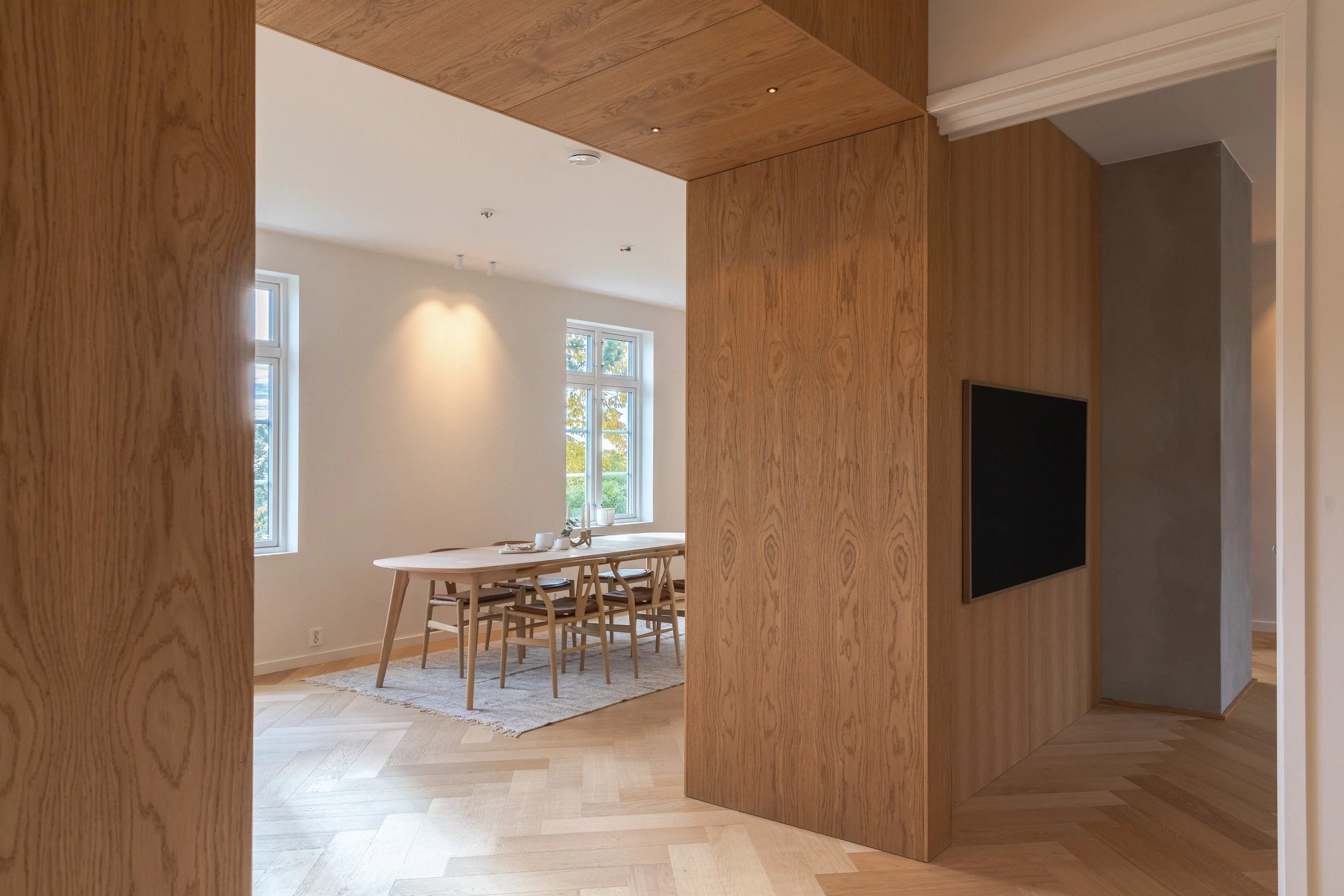 Finéroverflatene i elementveggen skaper en portal i overgangen mellom gangen og det store oppholdsrommet. Peisinnsatsen skyter gjennom veggen og utgjør et dekorativt varmebærende element.