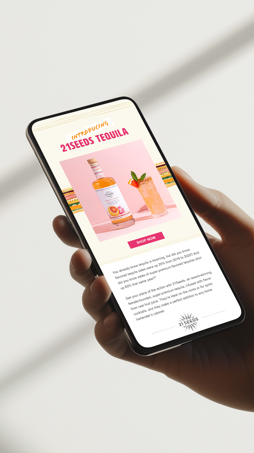 Hand holding a smartphone displaying an email advertisement for 21 Seeds Tequila with a bottle and a cocktail on a pink background, and a 'Shop Now' button.