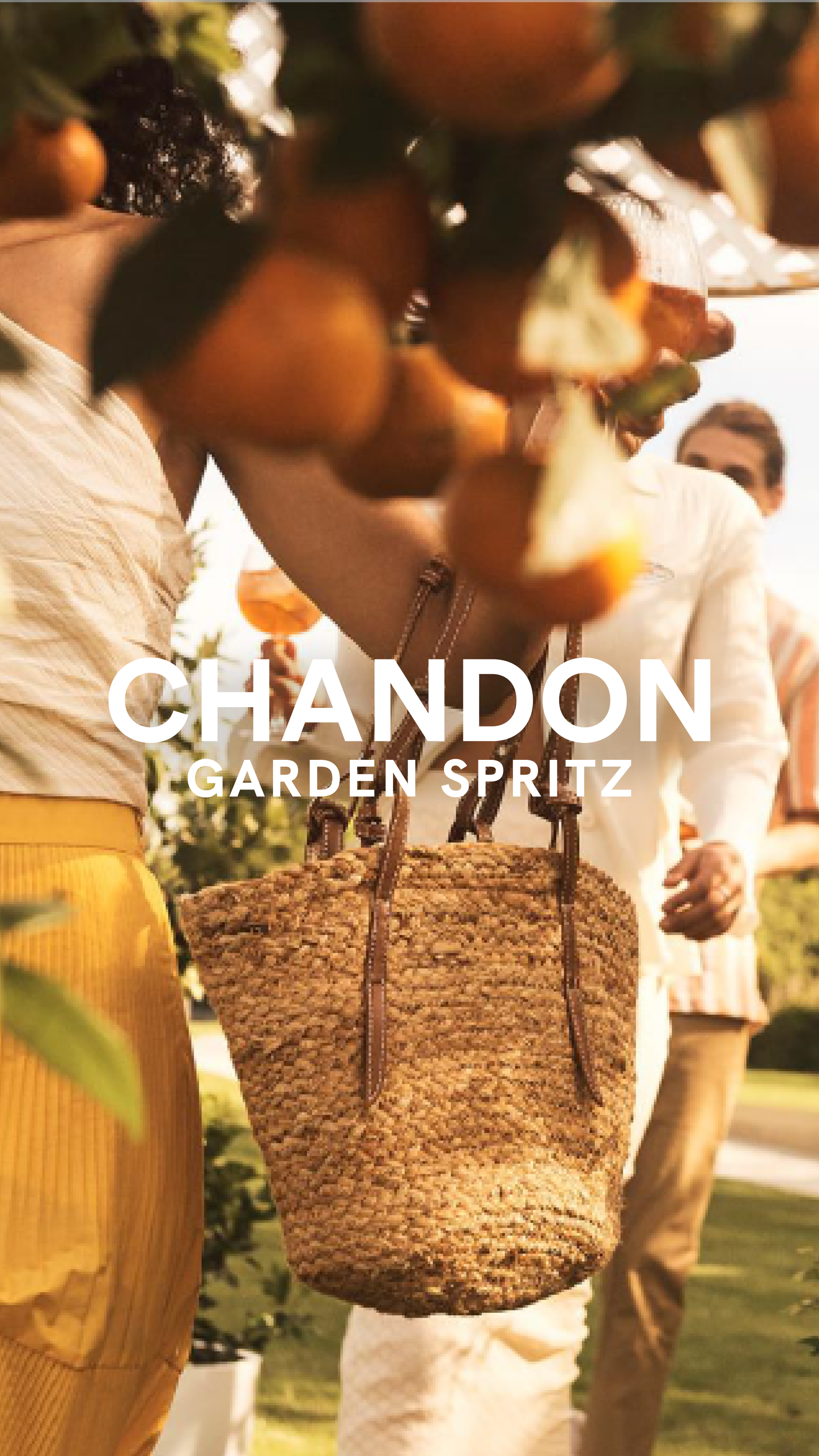 A sunlit outdoor scene with two people holding drinks. A straw bag hangs from one arm. Orange fruits dangle overhead. The words 'Chandon Garden Spritz' are centered on the image.