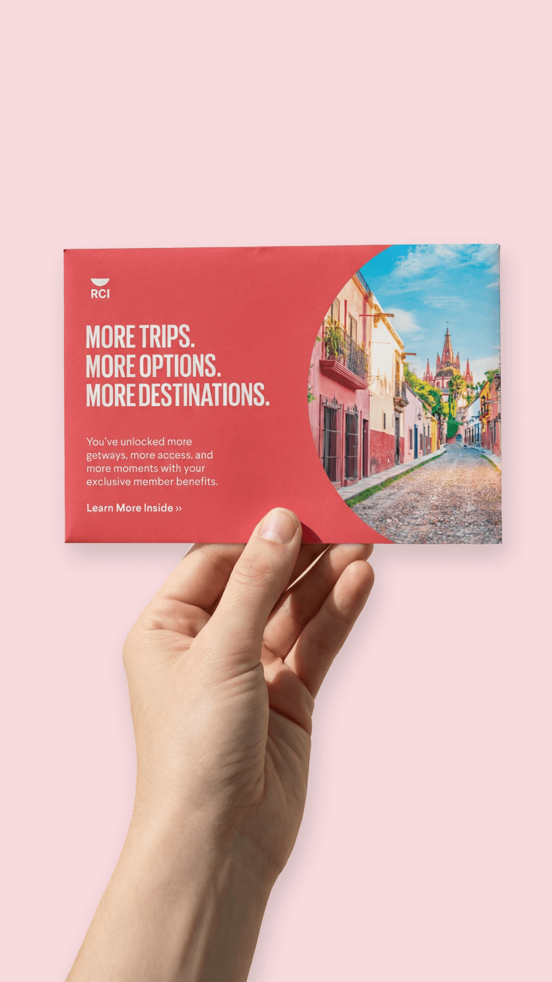 Hand holding a travel brochure with colorful buildings and a church in the distance against a pink background.