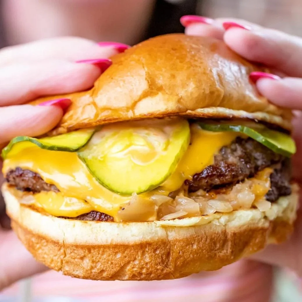 Close-up of a cheeseburger with pickles, lettuce, melted cheese, and a toasted bun.