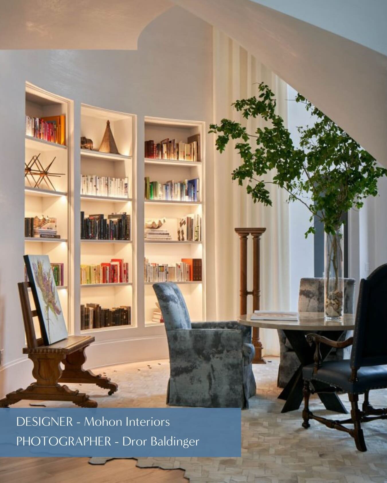 This space, embraced within plaster walls and graced with elegant drapery, provides undeniable warmth and comfort. The glowing nature of the lit built-in bookcases beckons to select a book and take a seat to indulge in its pages. Vased atop the table