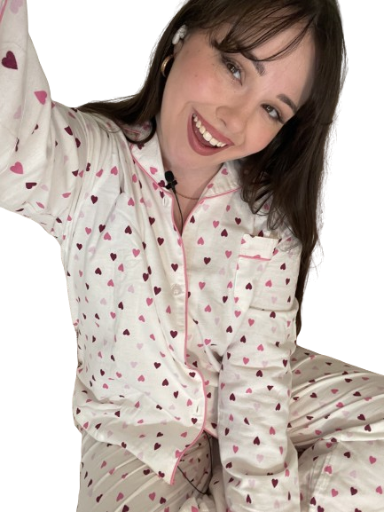 Woman smiling in heart-patterned pajamas, wearing earbuds, with a microphone clip on her shirt.
