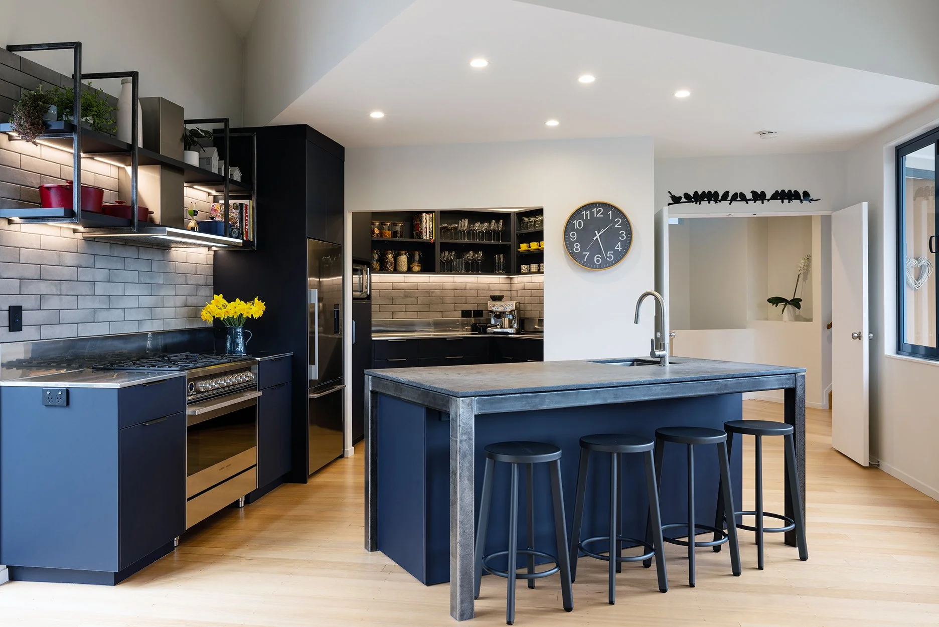 Modern kitchen with black cabinets, stainless steel appliances, open shelves, a kitchen island with seating, and a clock on the wall.