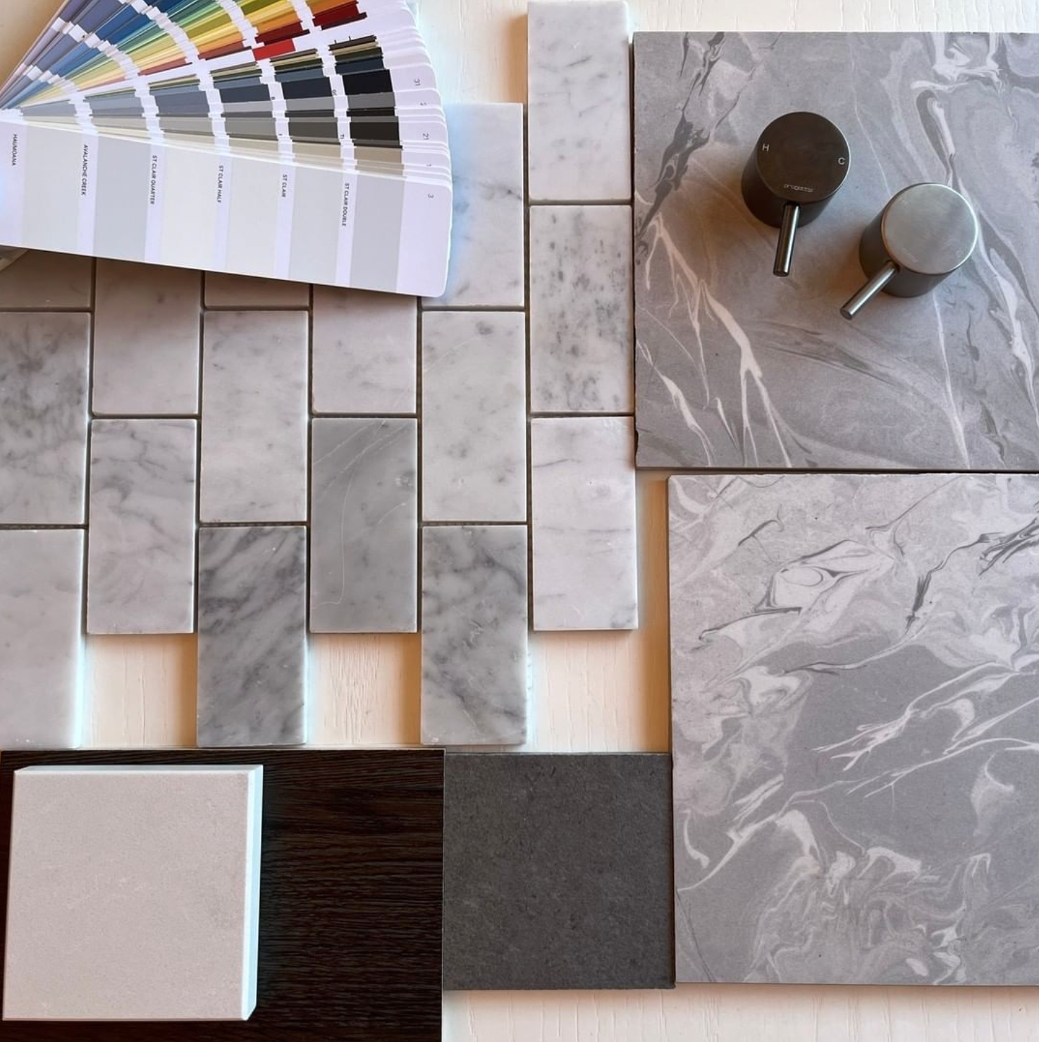 Sample of marble and tile material options for interior design, including marble tiles, small square tiles, larger slabs, and color swatches with a paint color sample fan deck.