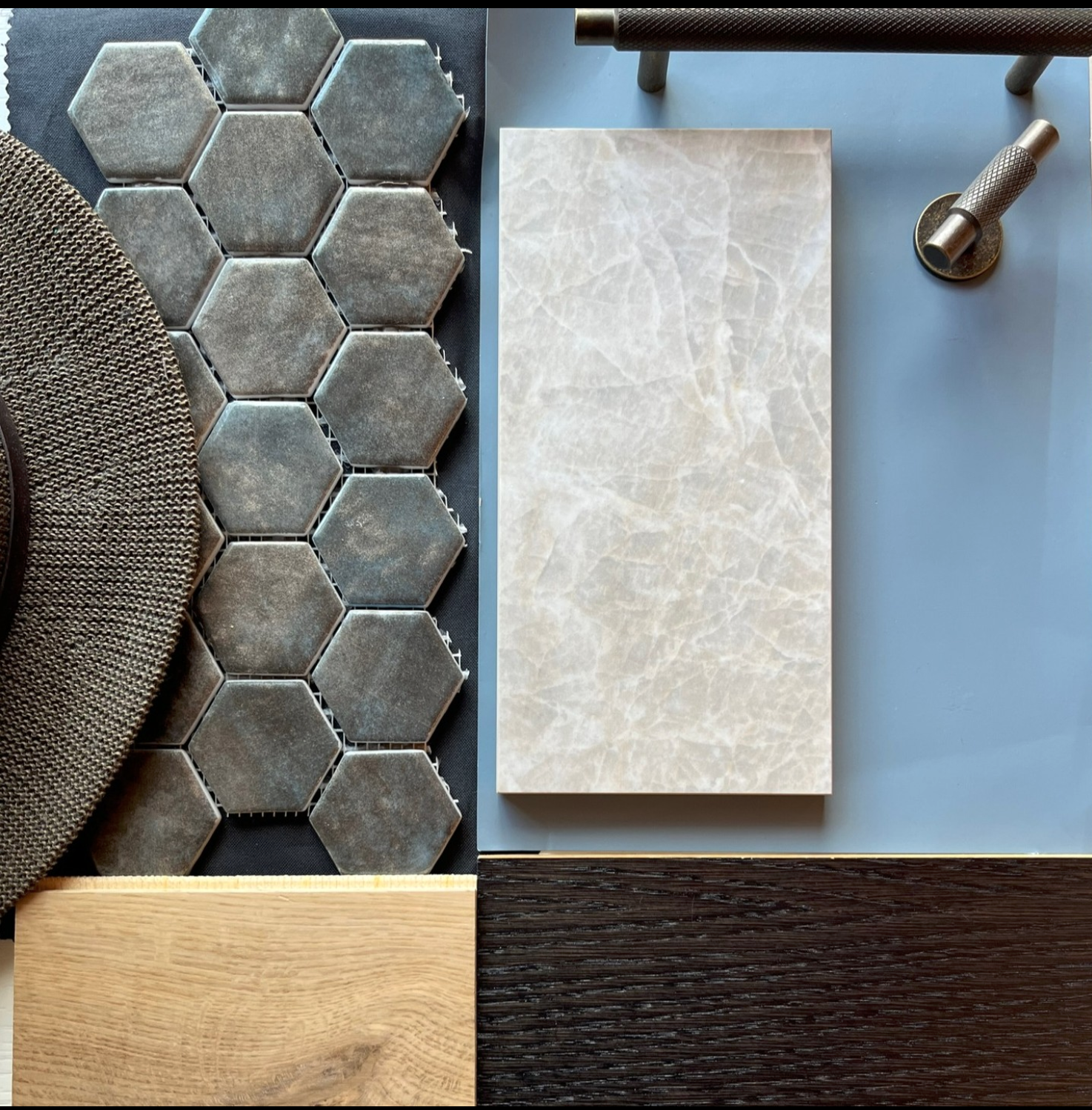 A collection of material samples including gray hexagonal tiles, a beige marble slab, a dark wood sample, a round textured mat, a wooden plank, a metallic object, and a light blue surface.
